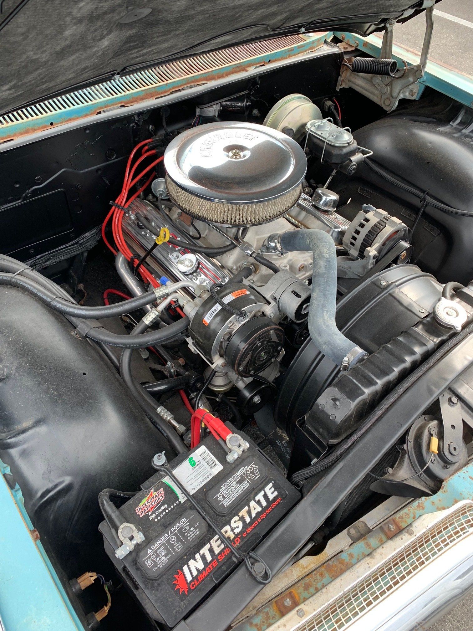 Chrome engine in a car bay, with black hoses and red wires visible, showing the engine compartment.