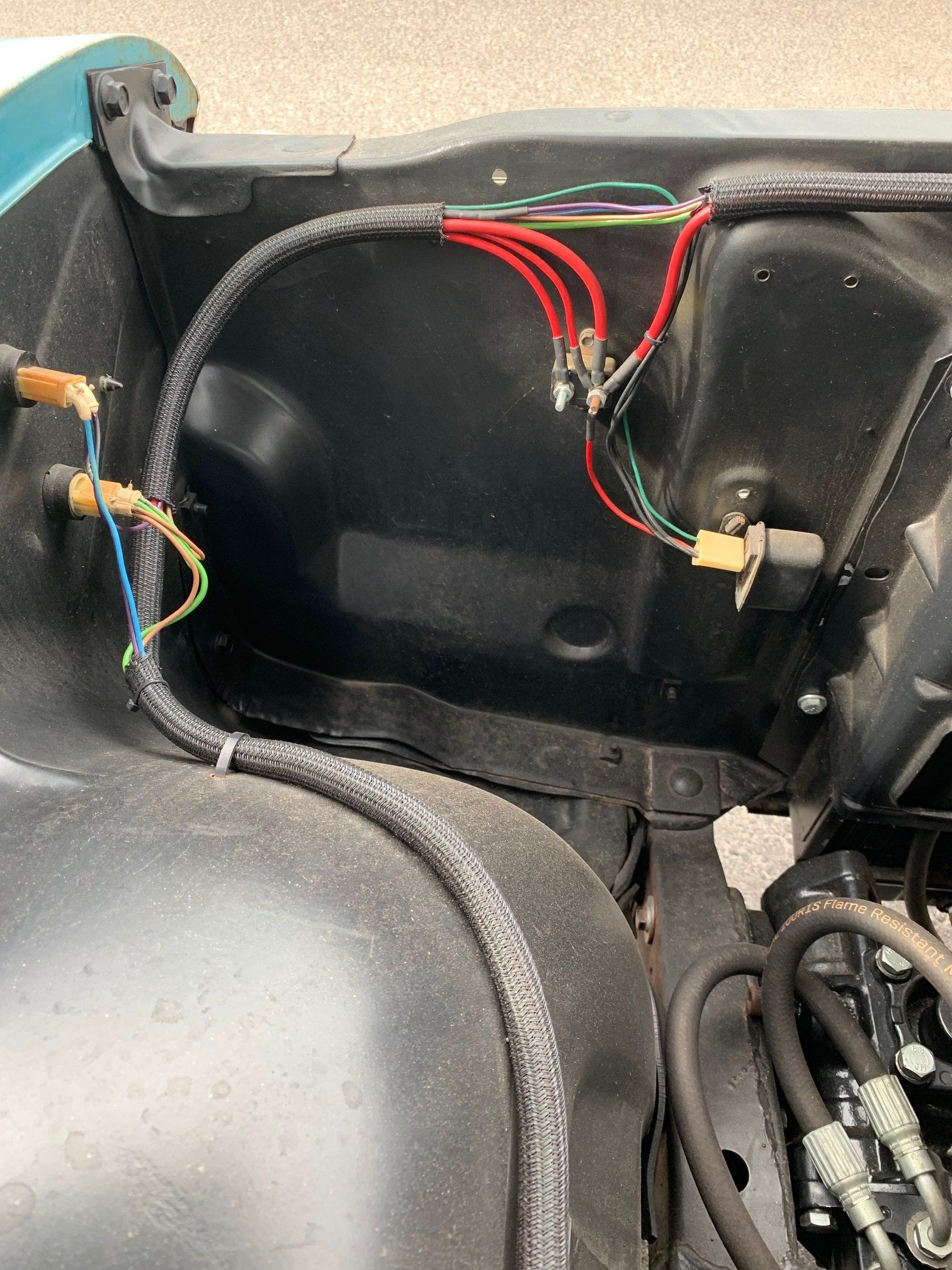 Close-up of car interior wiring in a black compartment, with red, green, and yellow wires and connectors.