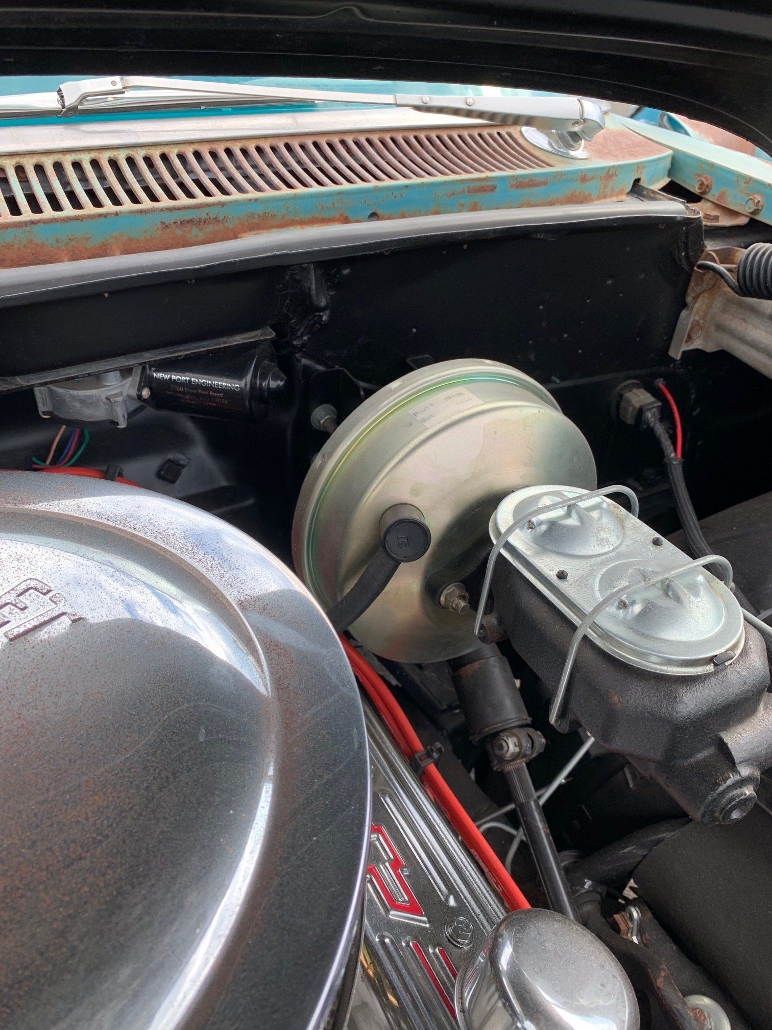 Close-up of a car engine bay with chrome air cleaner and brake booster, showing teal bodywork.