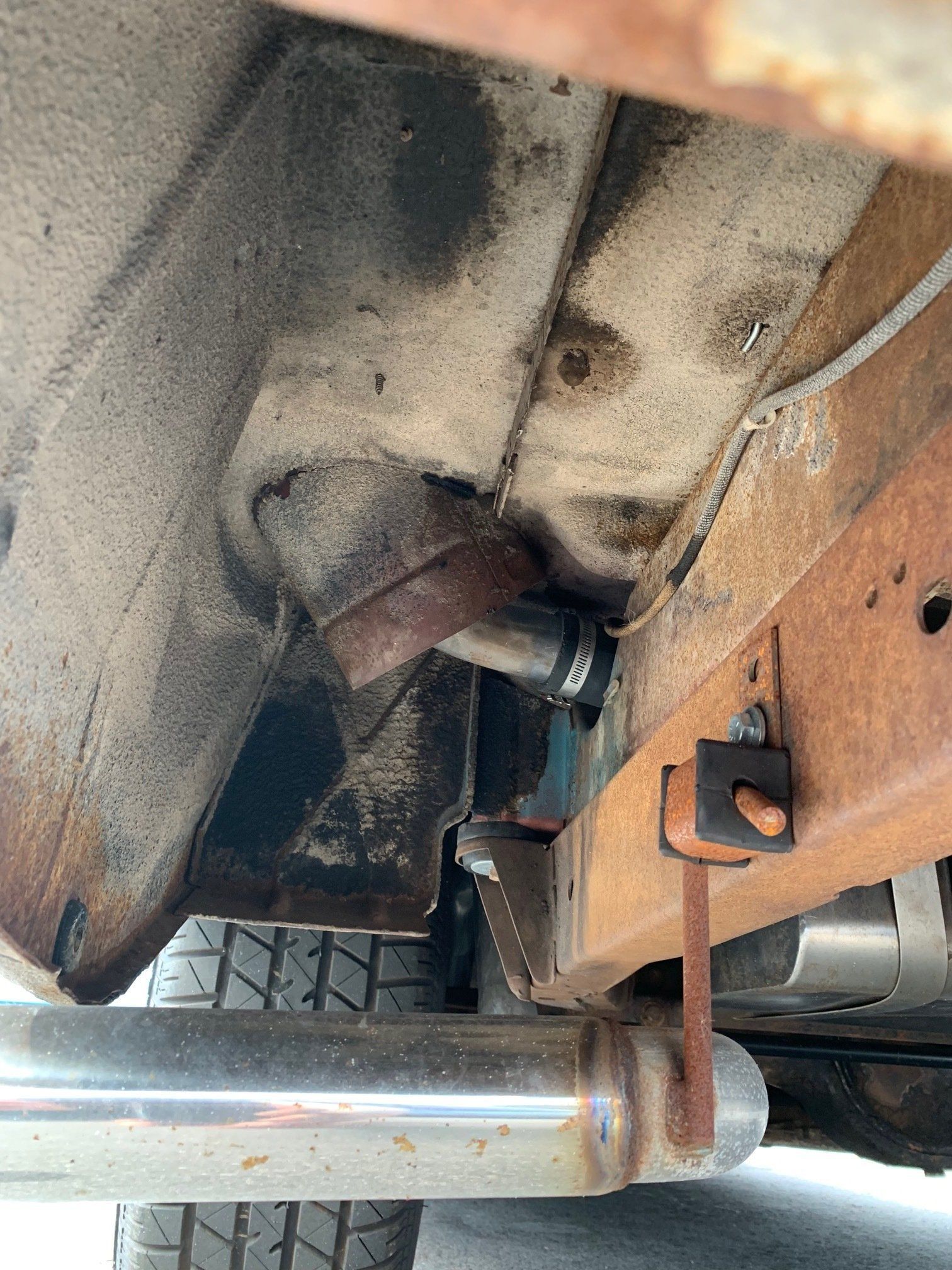 Undercarriage of a vehicle with a rusted exhaust pipe and muffler mount near the rear axle