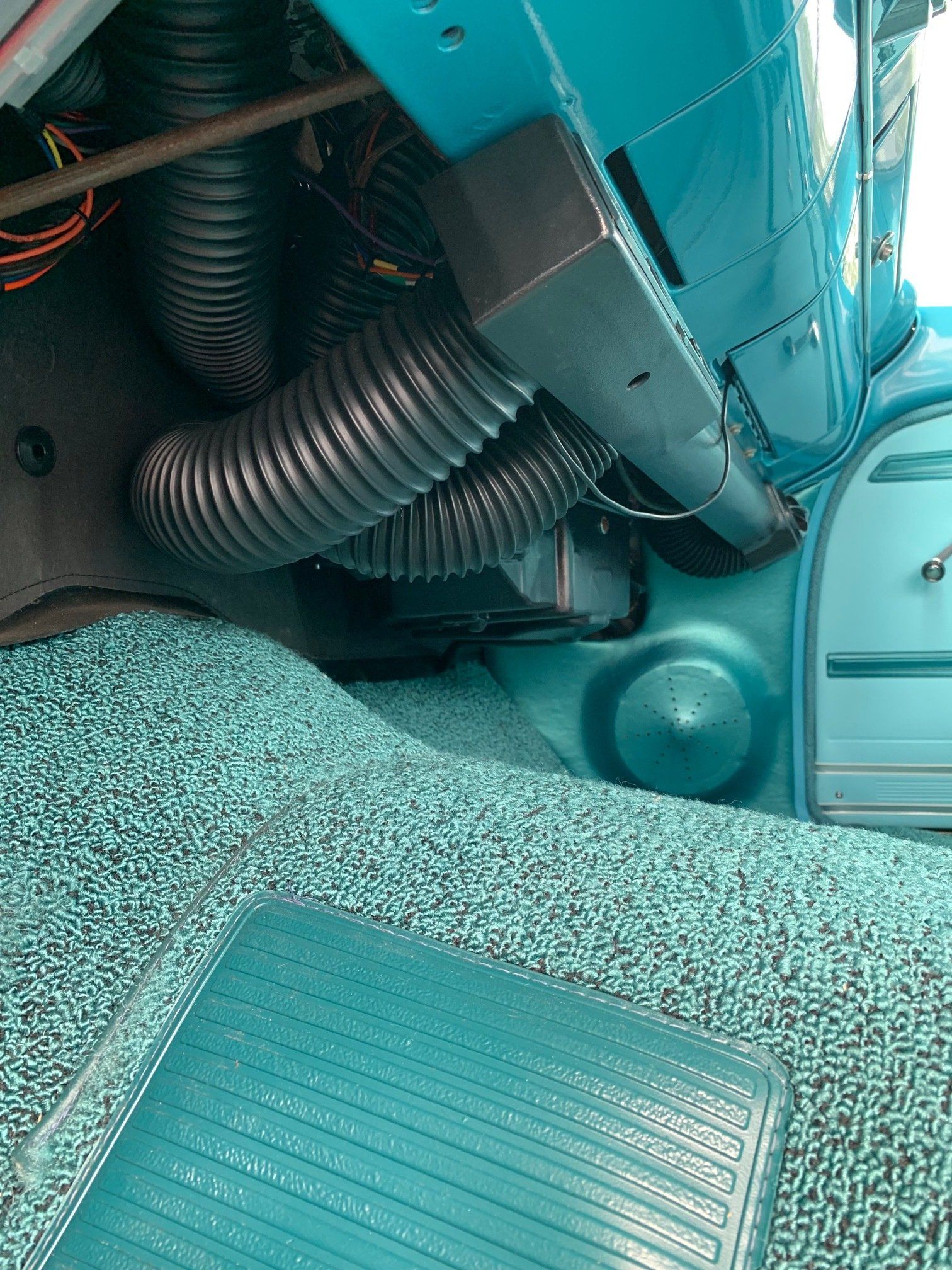 Close-up of a turquoise vehicle interior with black ribbed hoses and a textured floor panel