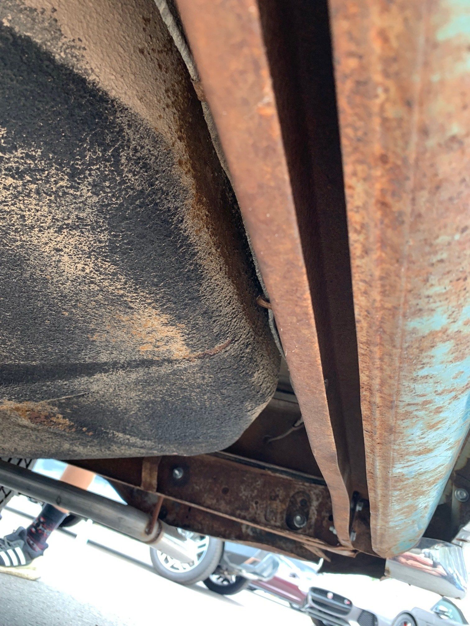 Close-up of a rusted metal underside of a vehicle with a black wheel and frame components visible.