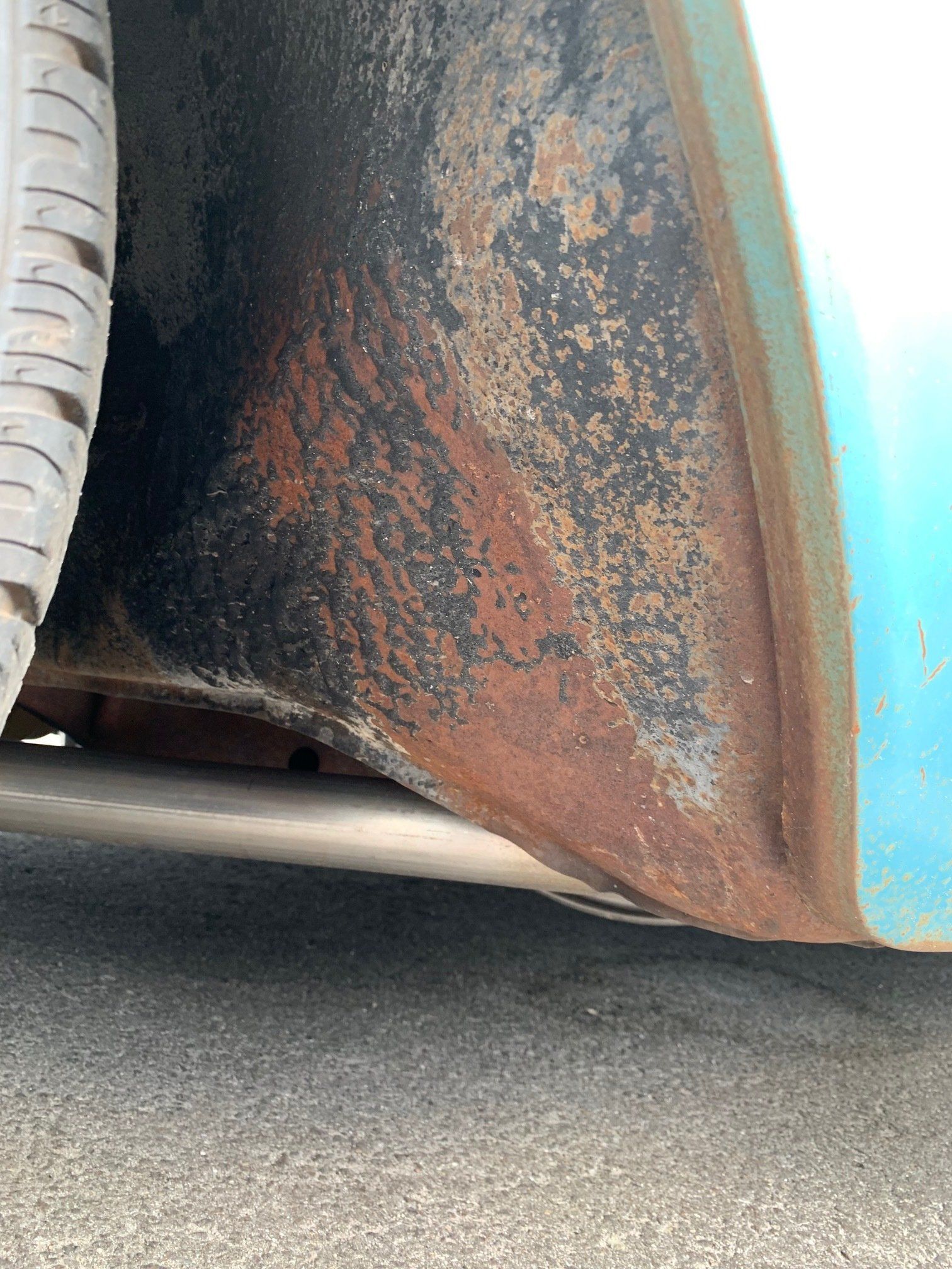 Close-up of a rusted car wheel arch and mud flap with tire on pavement