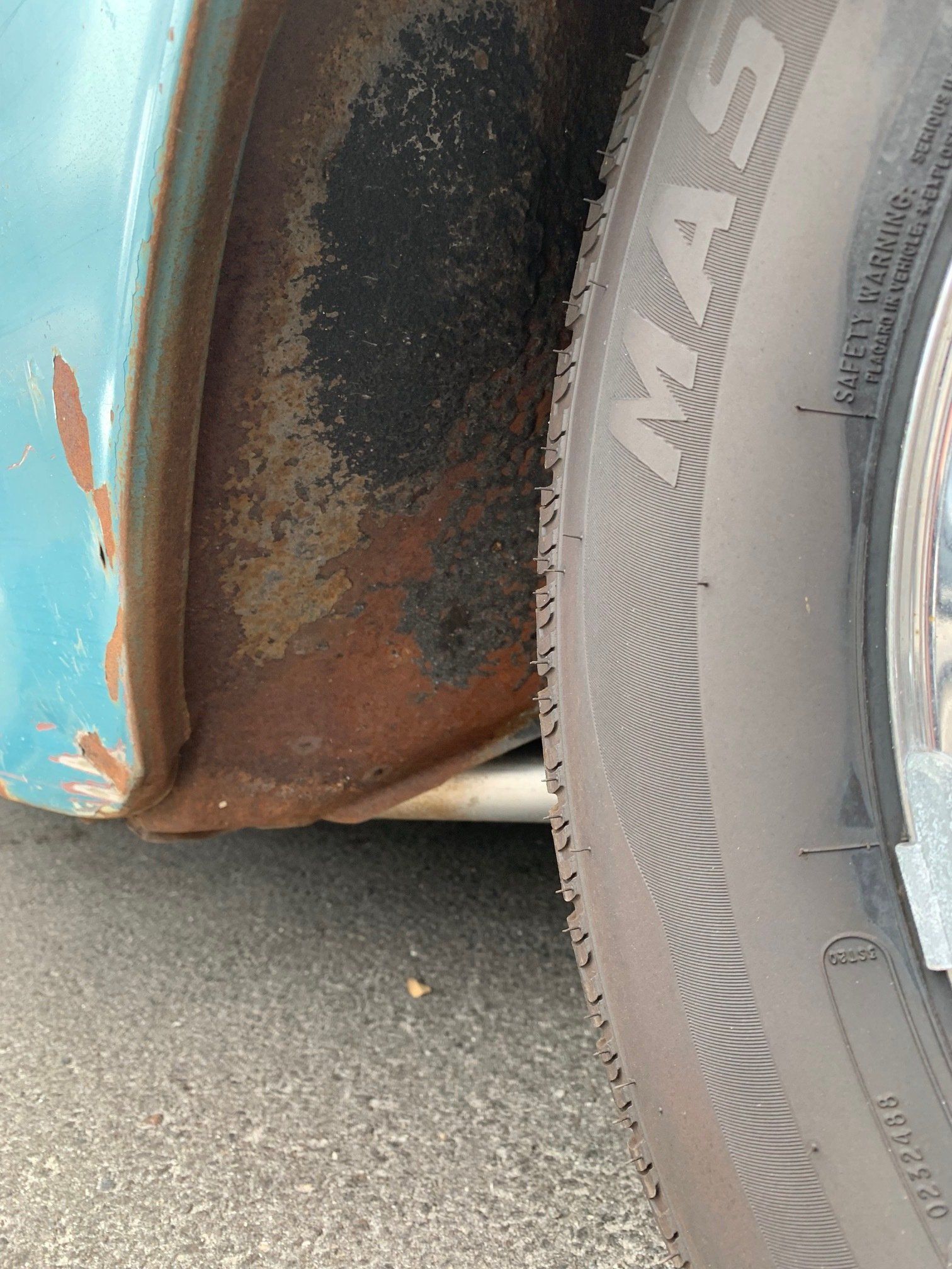 Close-up of a rusty car wheel well and tire on a blue vehicle, showing heavy corrosion