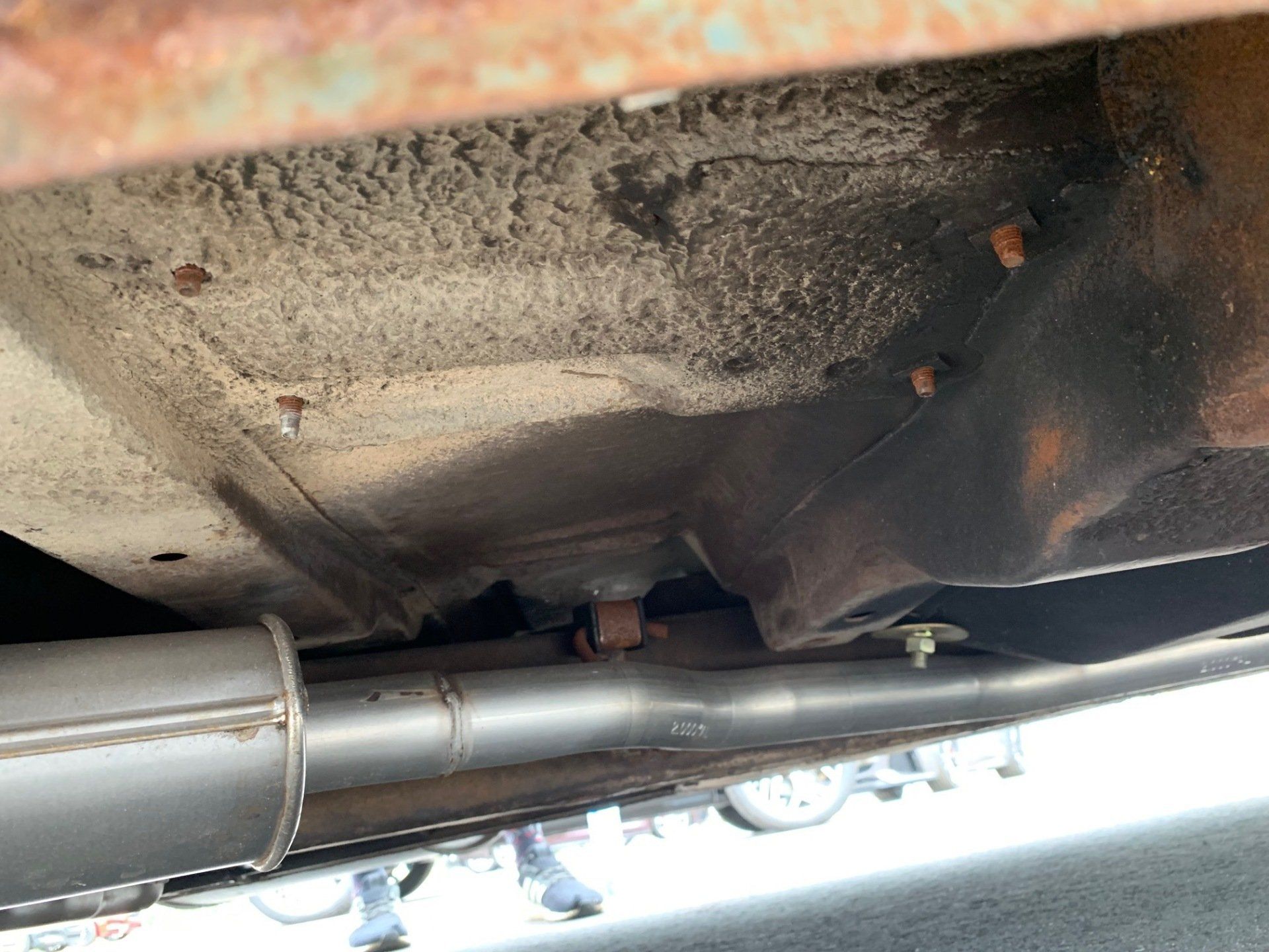 Undercarriage of a car with a rusty, dirt-stained floor pan and exhaust pipe visible