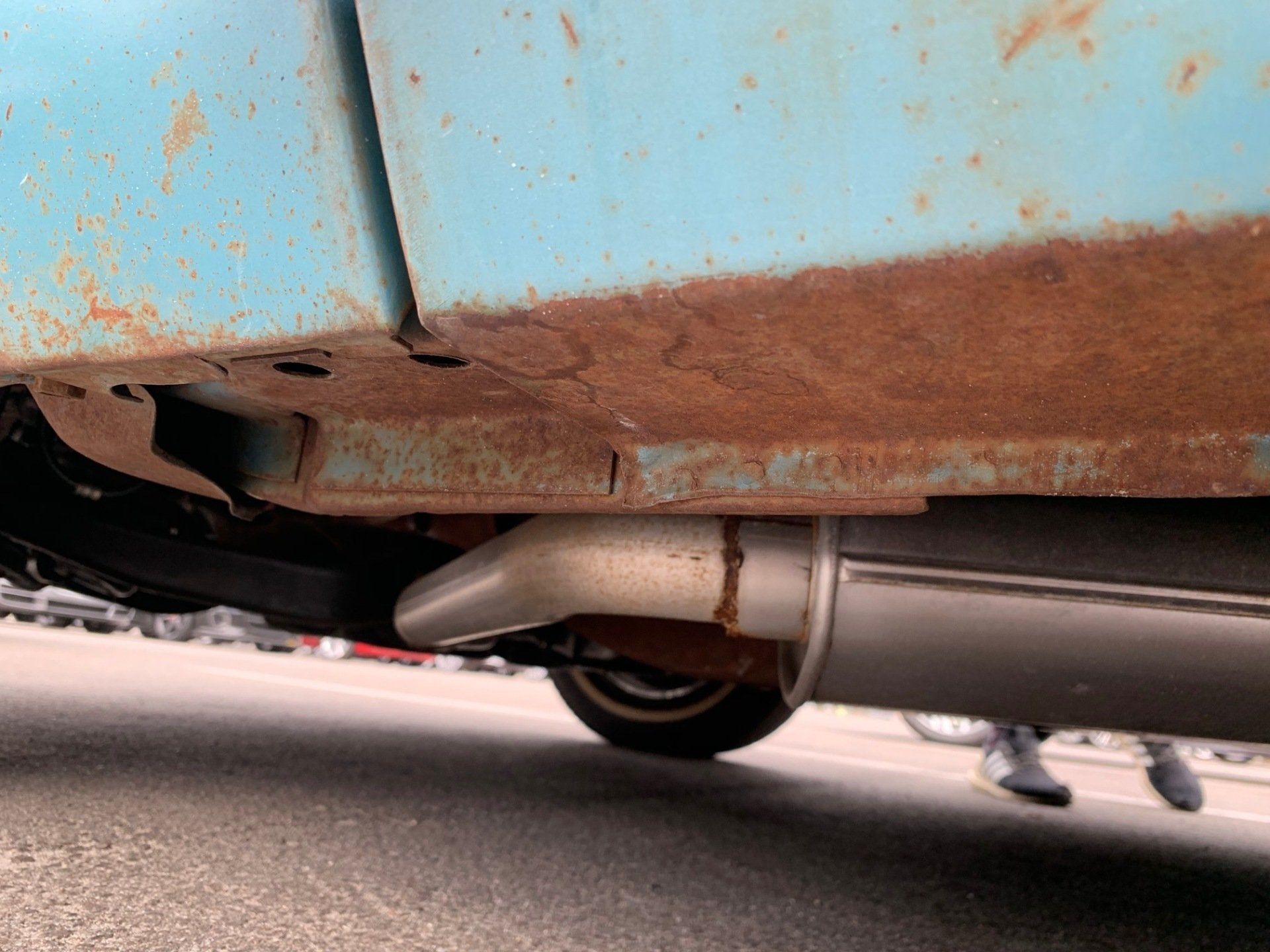 Rusty blue car underside with exhaust pipe and rear wheel close to the ground