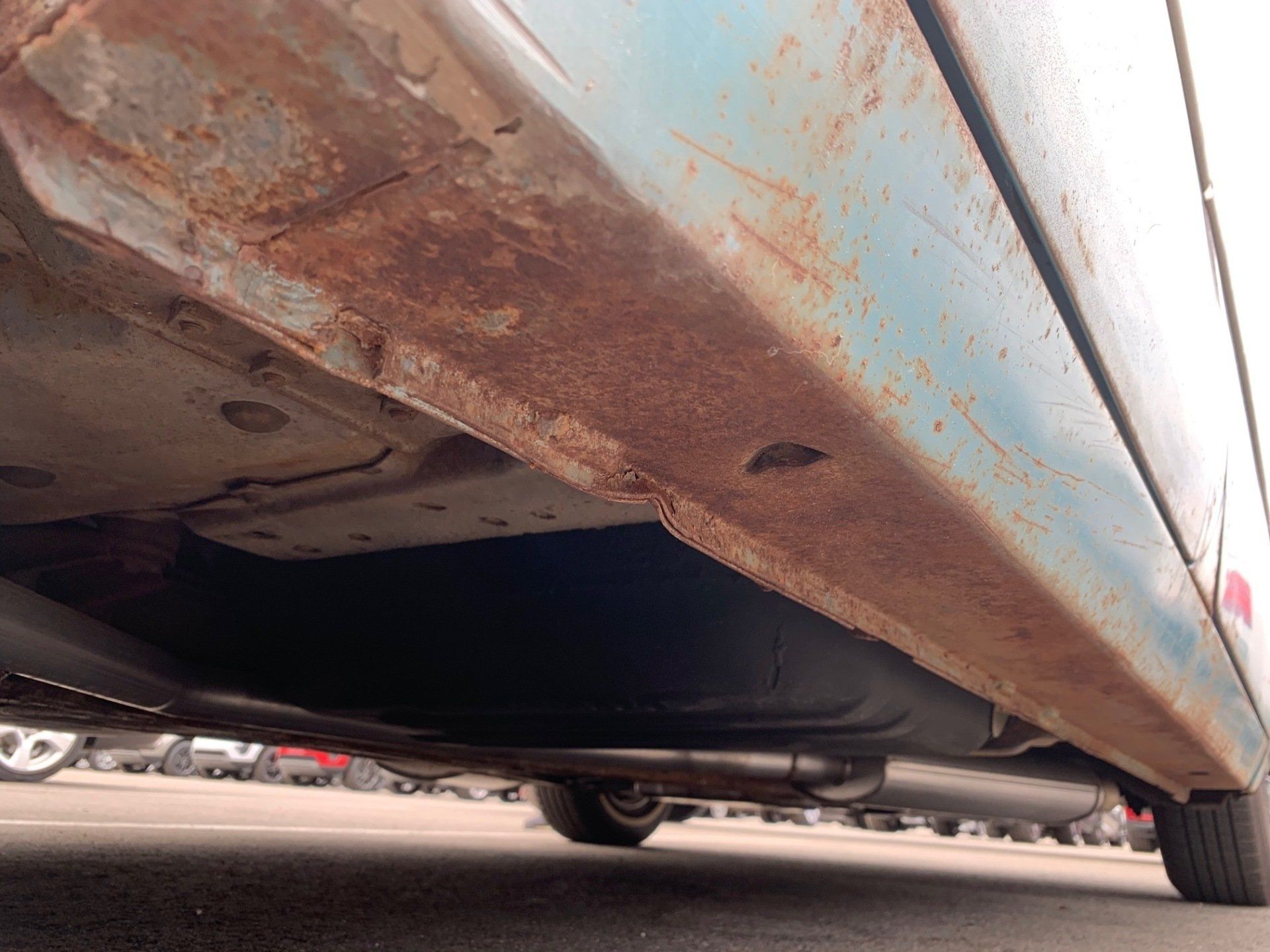 Rusty, corroded underside of a vehicle parked close to the ground.