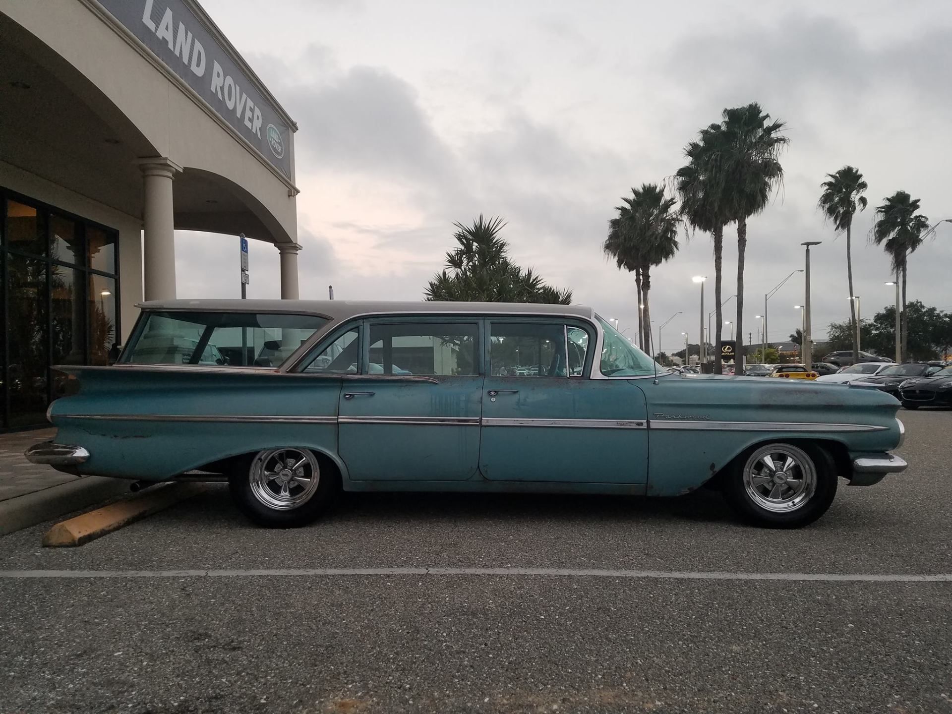 Turquoise vintage station wagon parked outside a Land Rover dealership at dusk