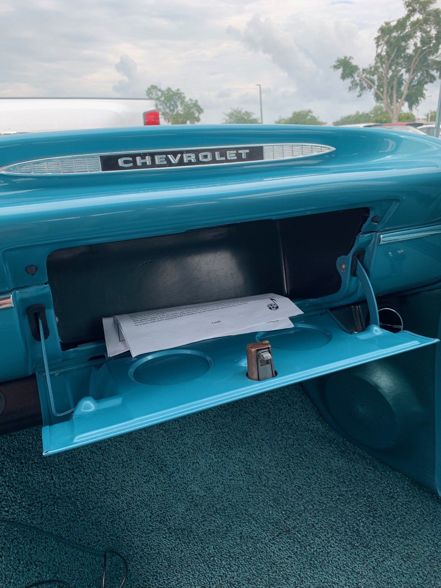 Open trunk of a turquoise Chevrolet with empty cargo area and license plate bracket visible