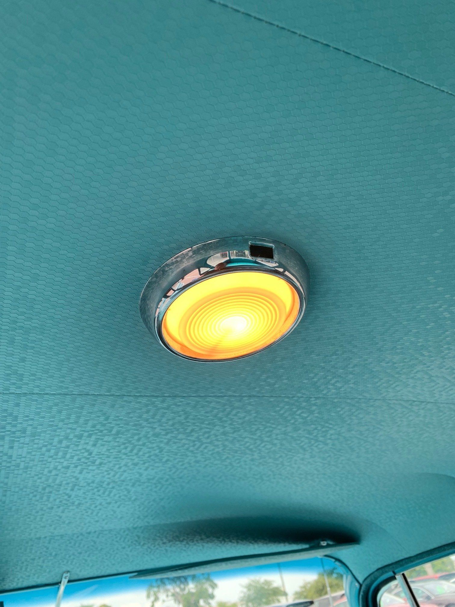 Yellow dome light mounted on a teal vehicle ceiling, with the top of a window visible below.
