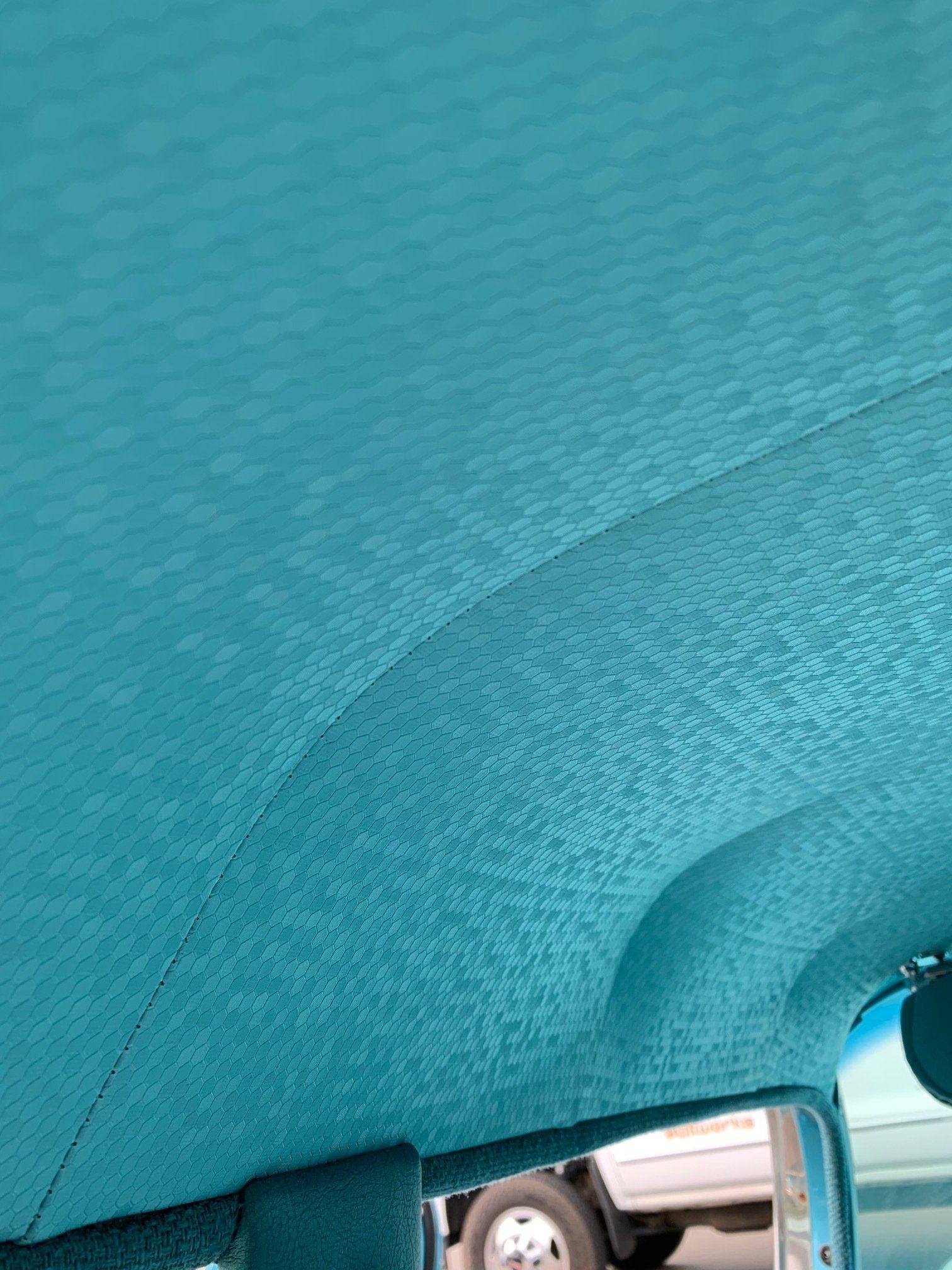 Close-up of a turquoise car interior roof and window frame with textured fabric.