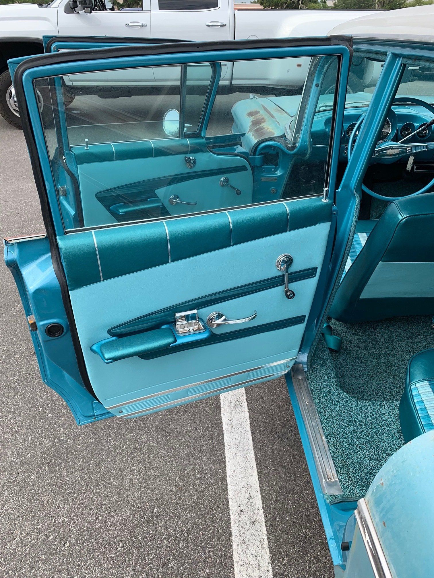 Open turquoise car door with teal interior, parked on pavement with white line visible.