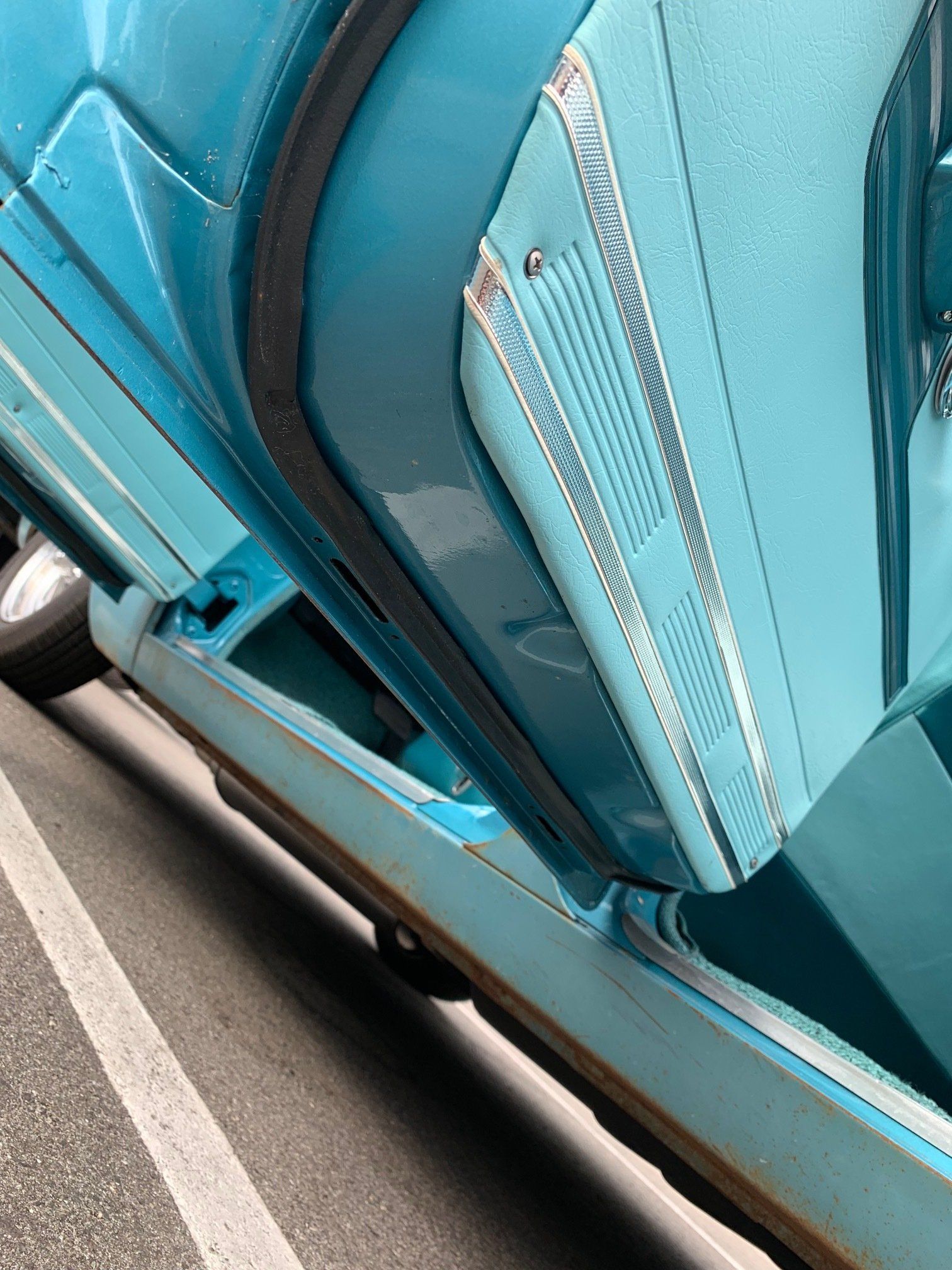Close-up of a turquoise vintage car’s chrome side vent and trim.