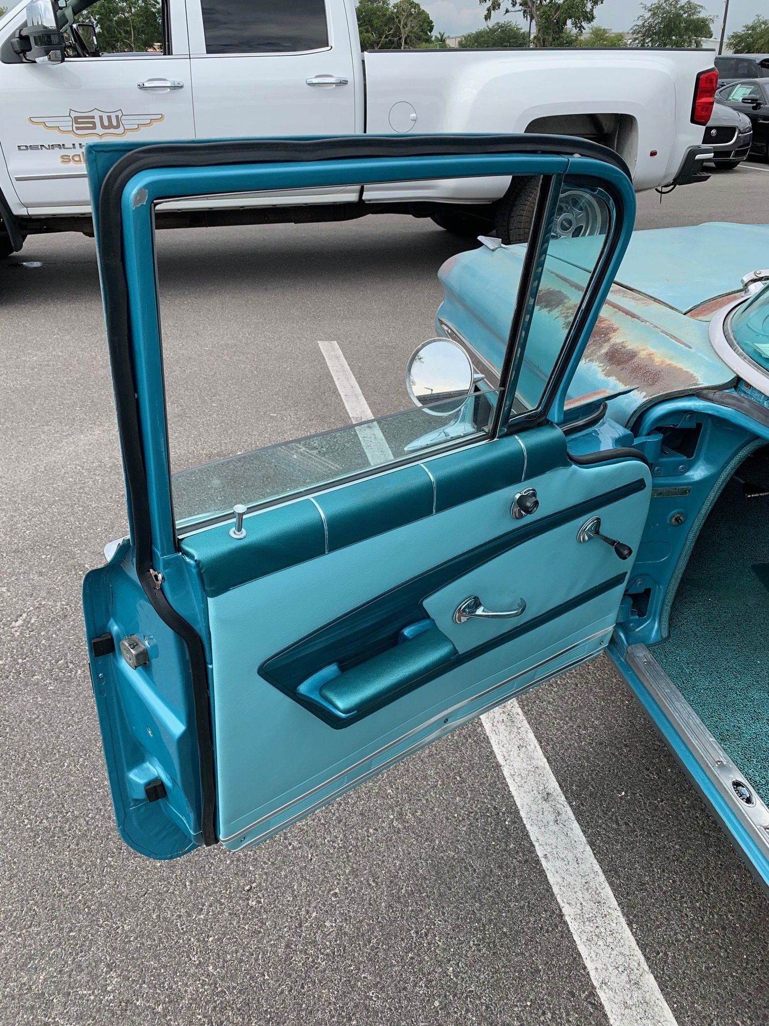 Open turquoise classic car door with chrome trim in a parking lot