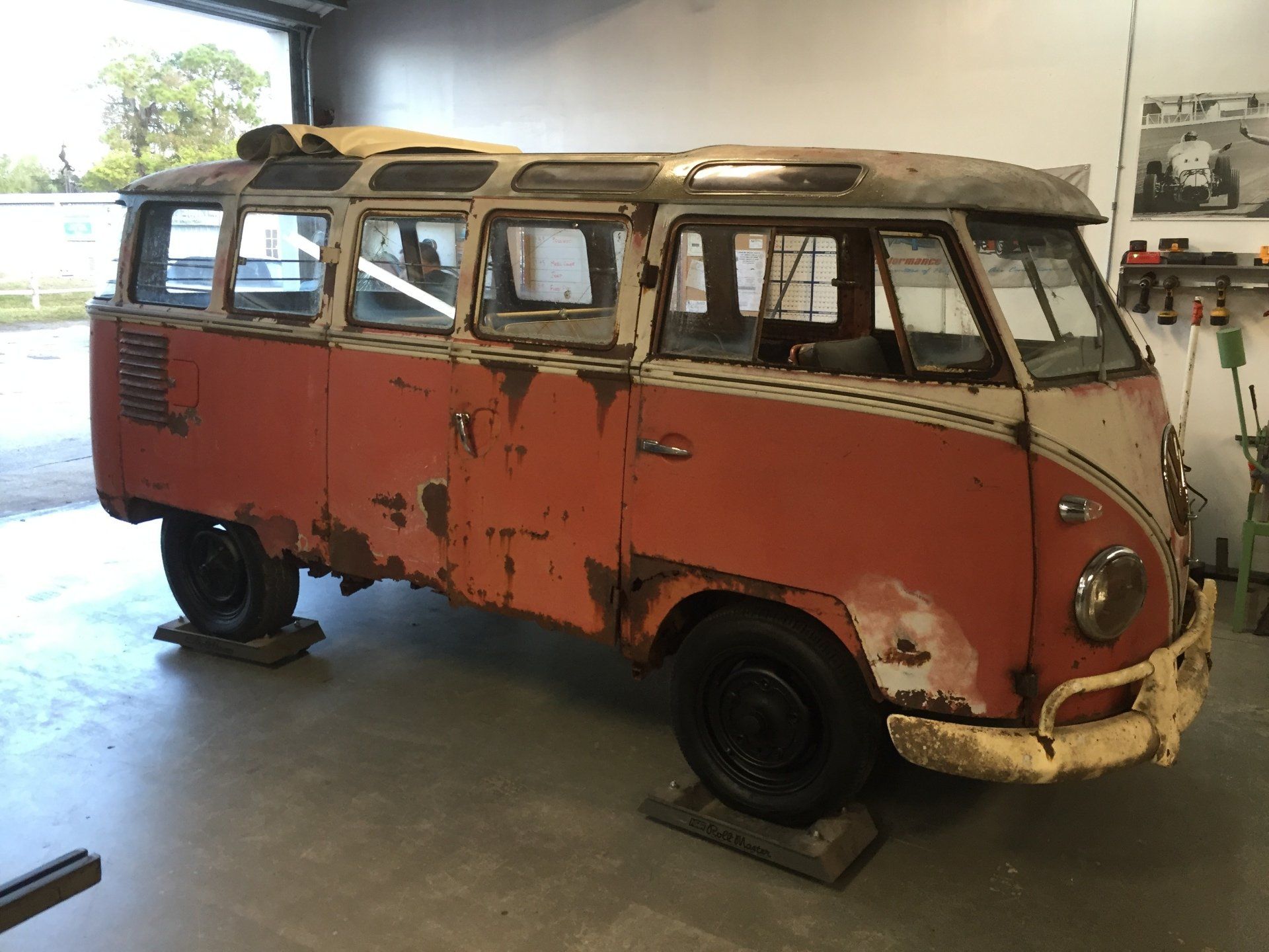 Rusty red vintage van in a garage, with peeling paint and worn body panels.