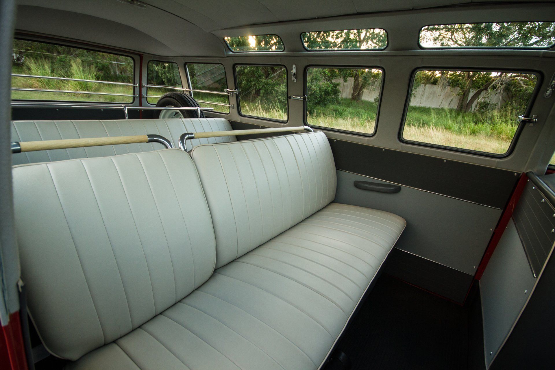 Interior of a vintage vehicle with light gray bench seats and large windows overlooking greenery