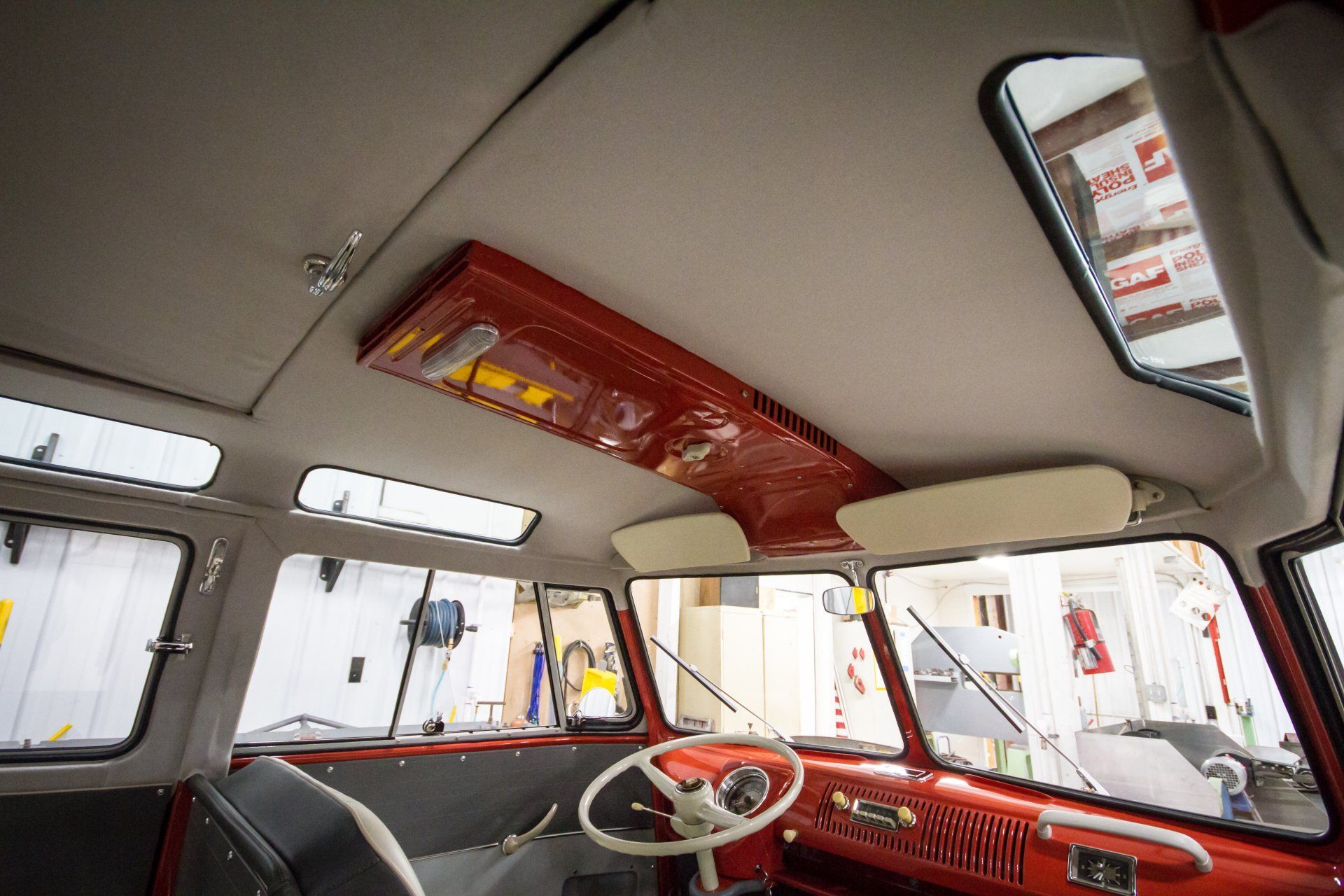Vintage car interior with red dashboard, white ceiling, and open windows, viewed from the back seat