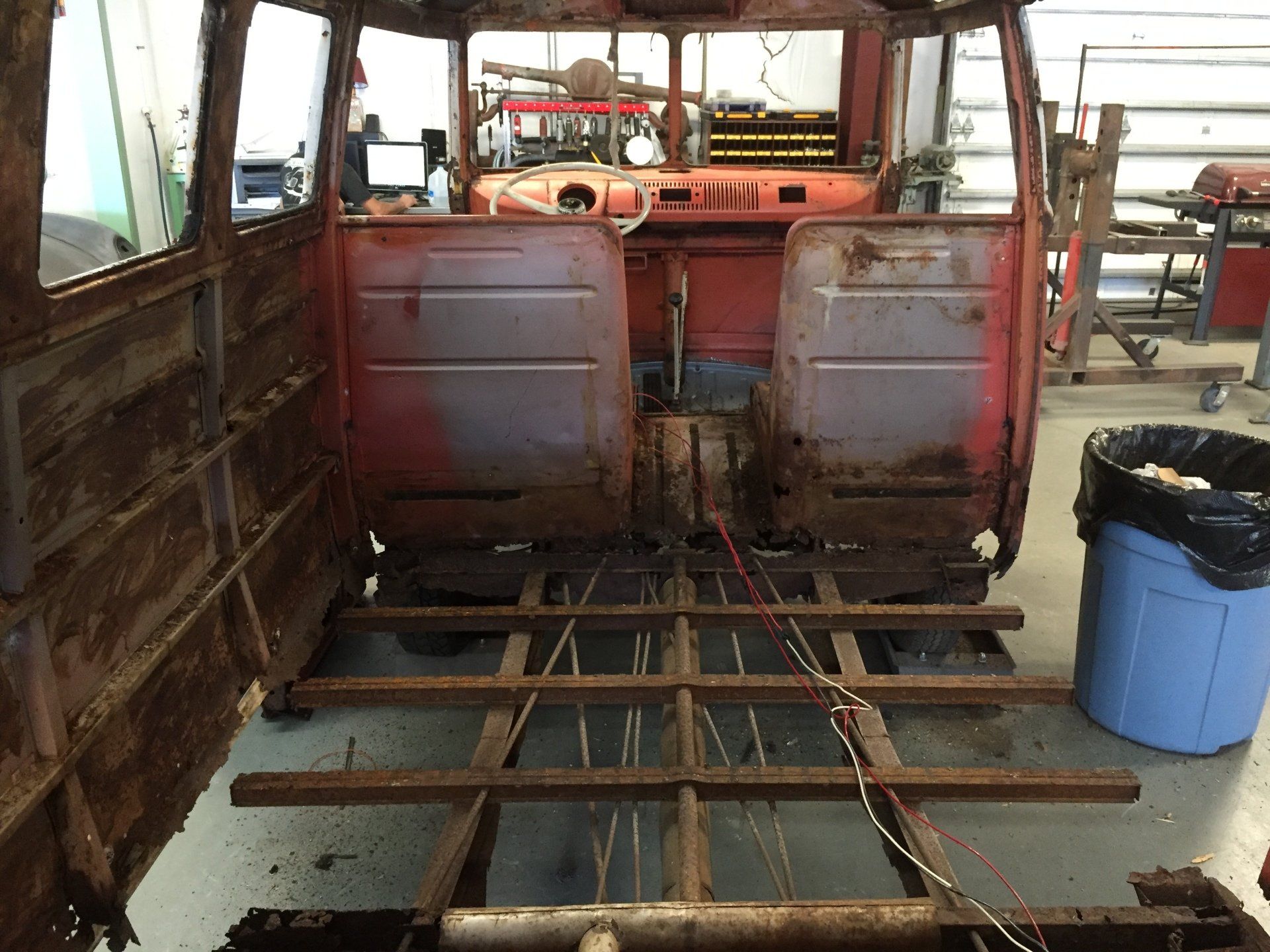 Rusty bus interior under repair, with exposed floor beams and worn red seats.
