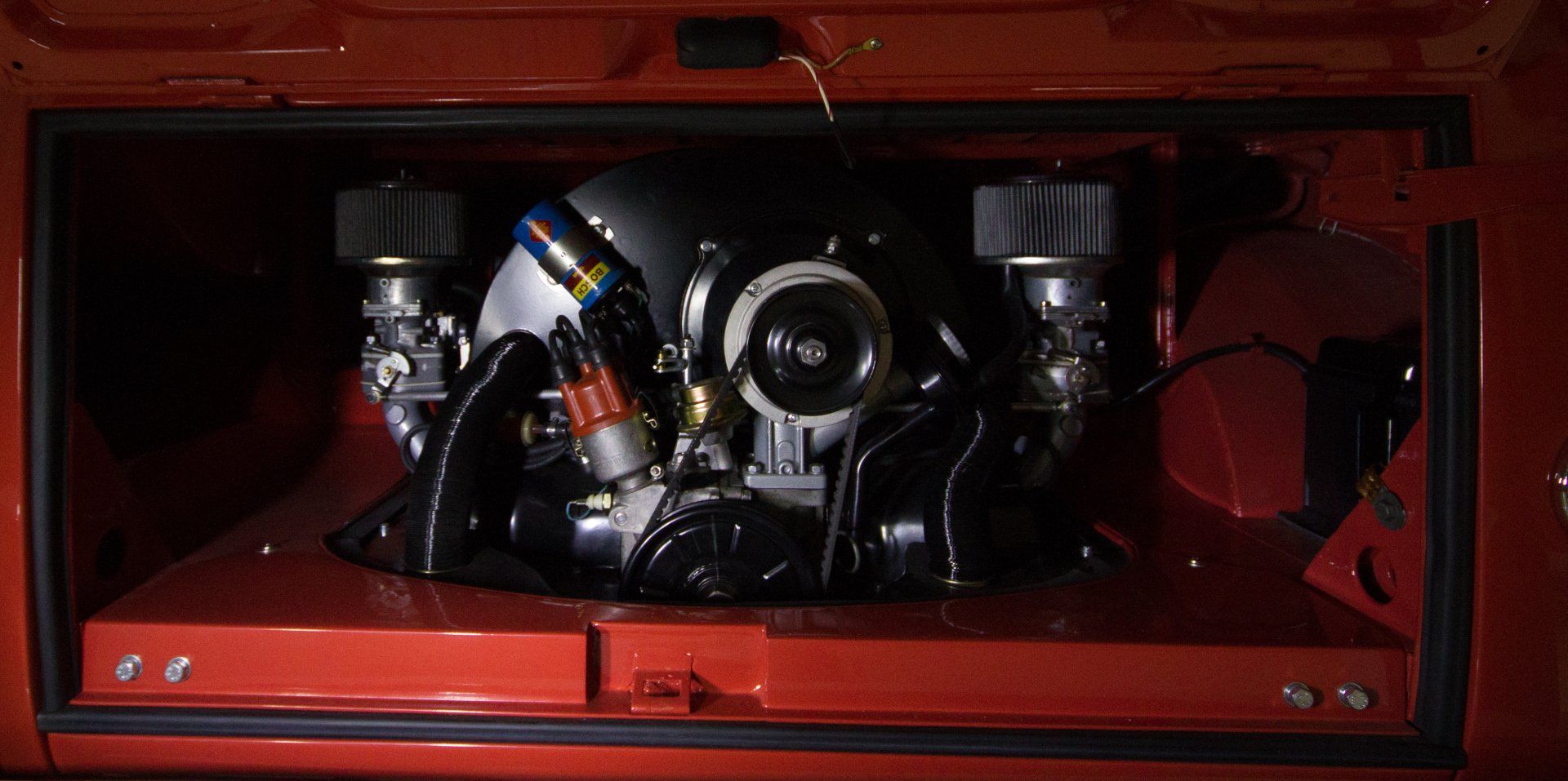 Red storage compartment holding assorted black and silver mechanical parts and a small canister