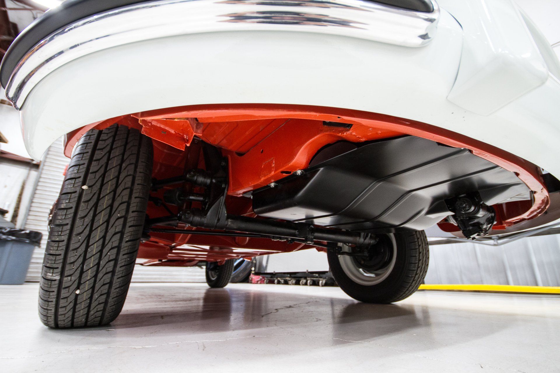 Underside of a vintage car with glossy red chassis and visible suspension in a garage