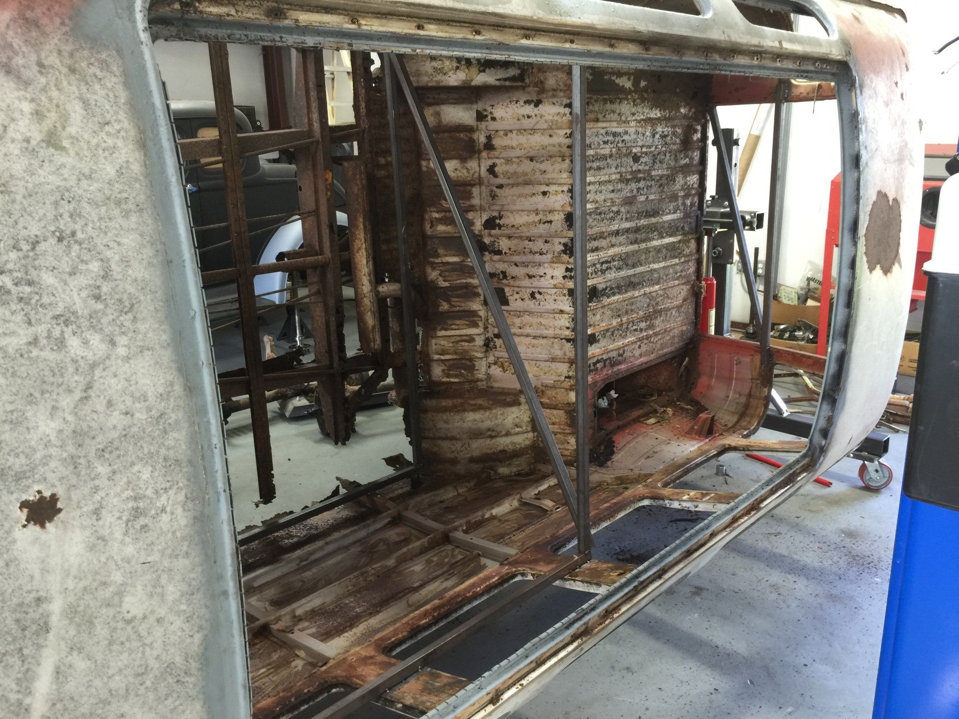 Damaged bus interior with exposed wooden frame and torn panels in a workshop
