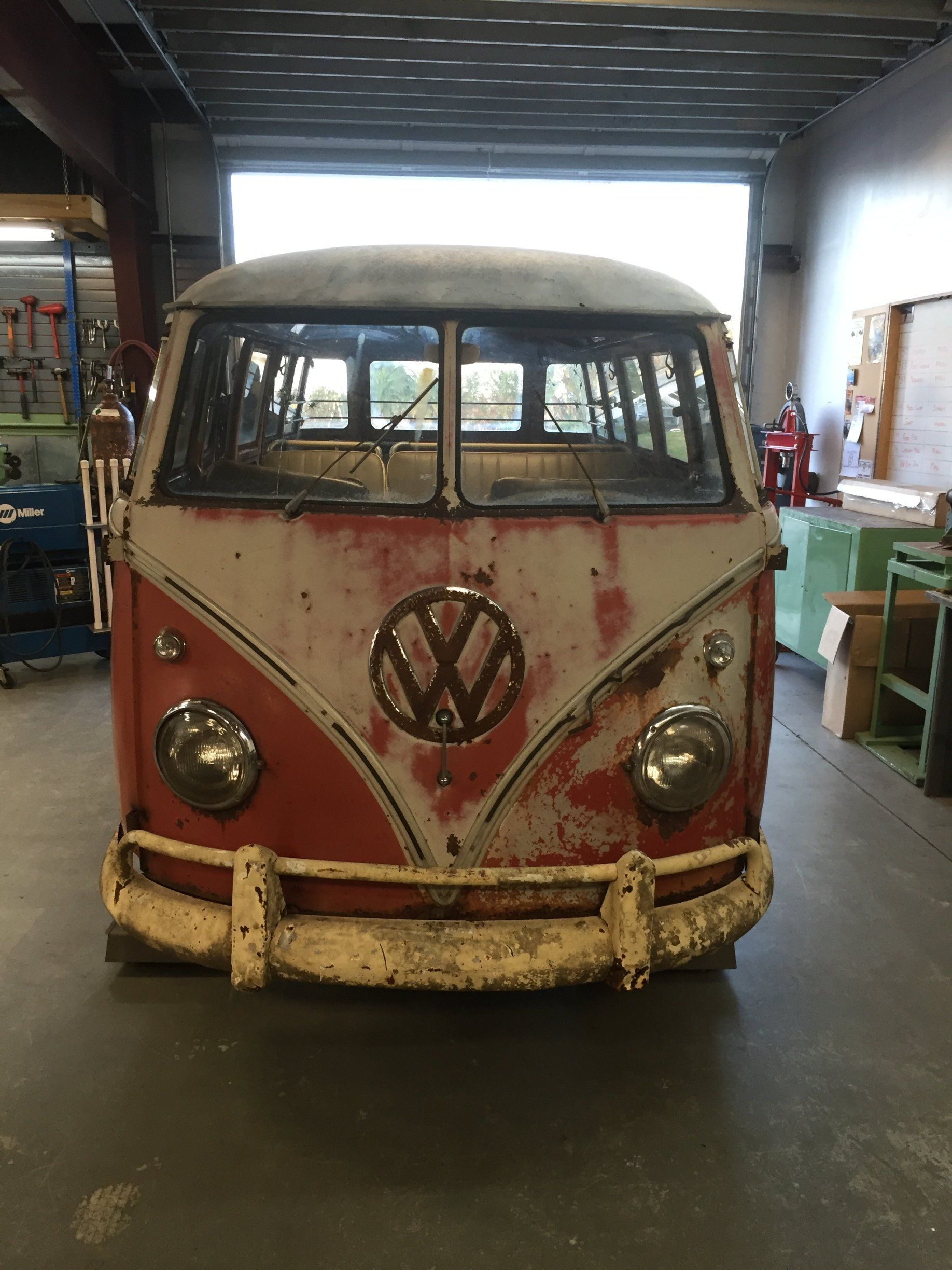 Rusty red and white vintage Volkswagen van parked indoors in a workshop.