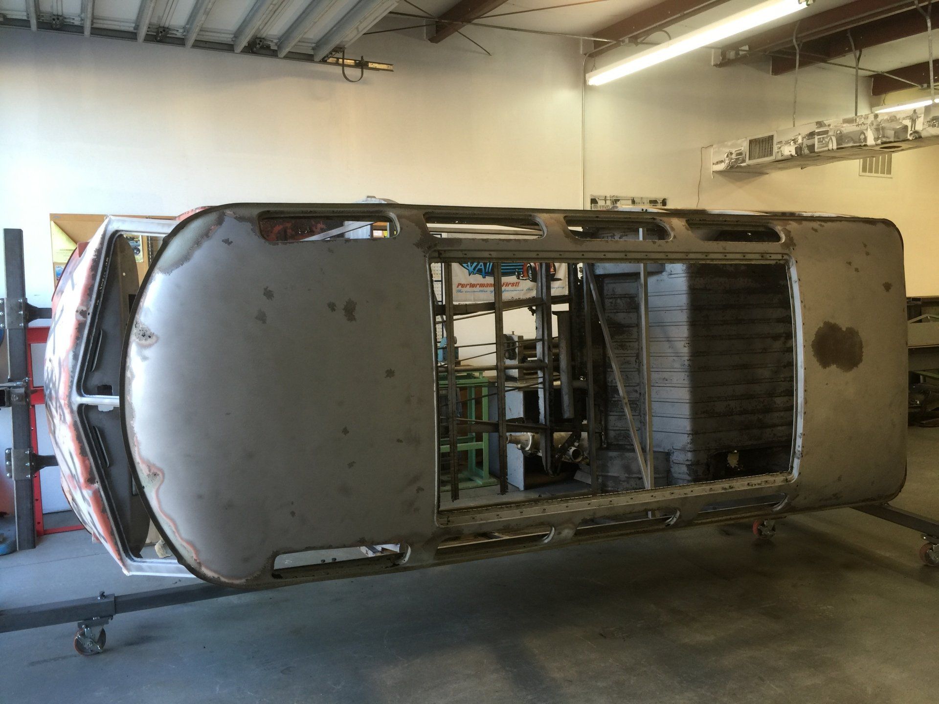Overturned silver car shell in a garage, showing exposed interior and missing panels