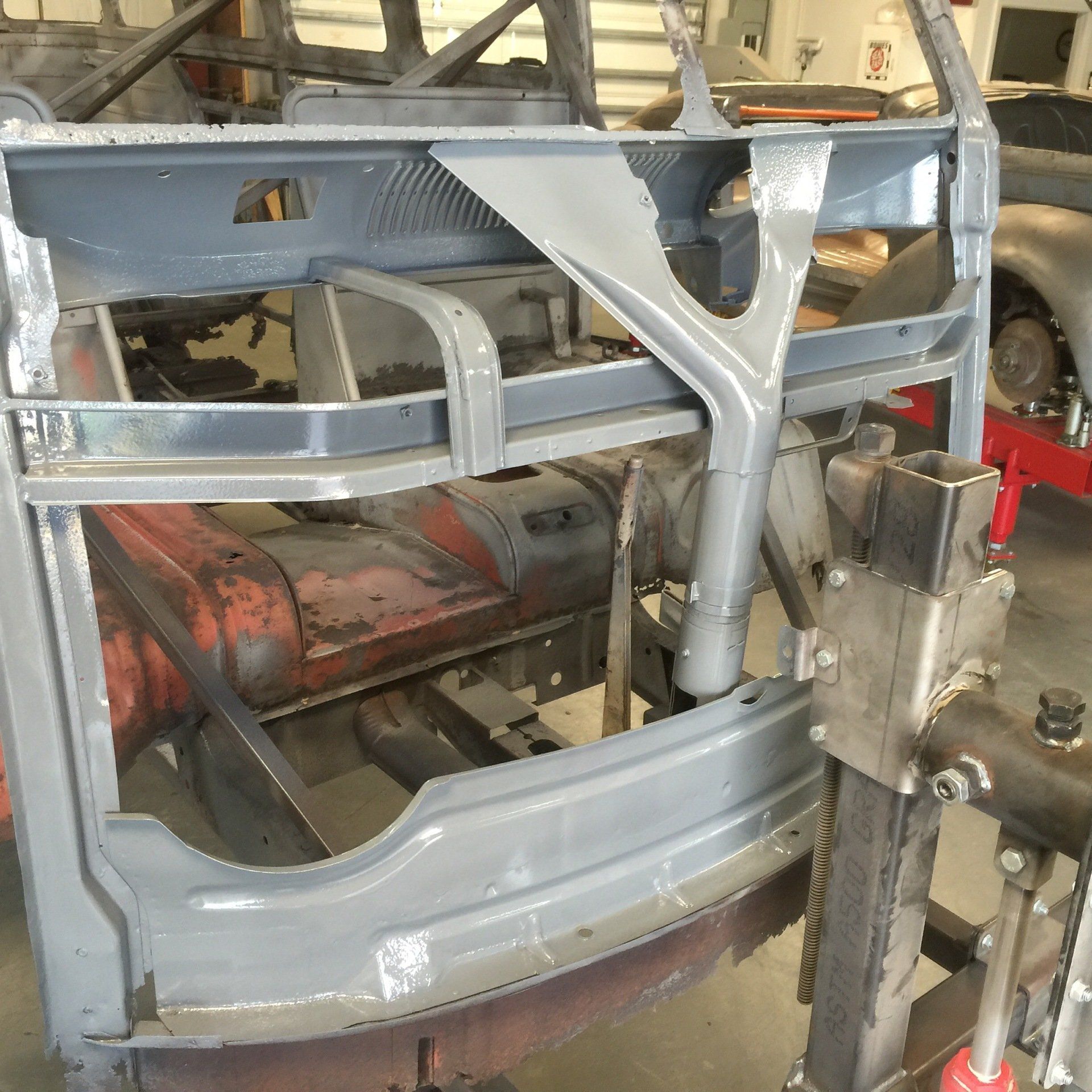 Gray car body frame in an auto repair shop, with welding equipment and metal support jig nearby