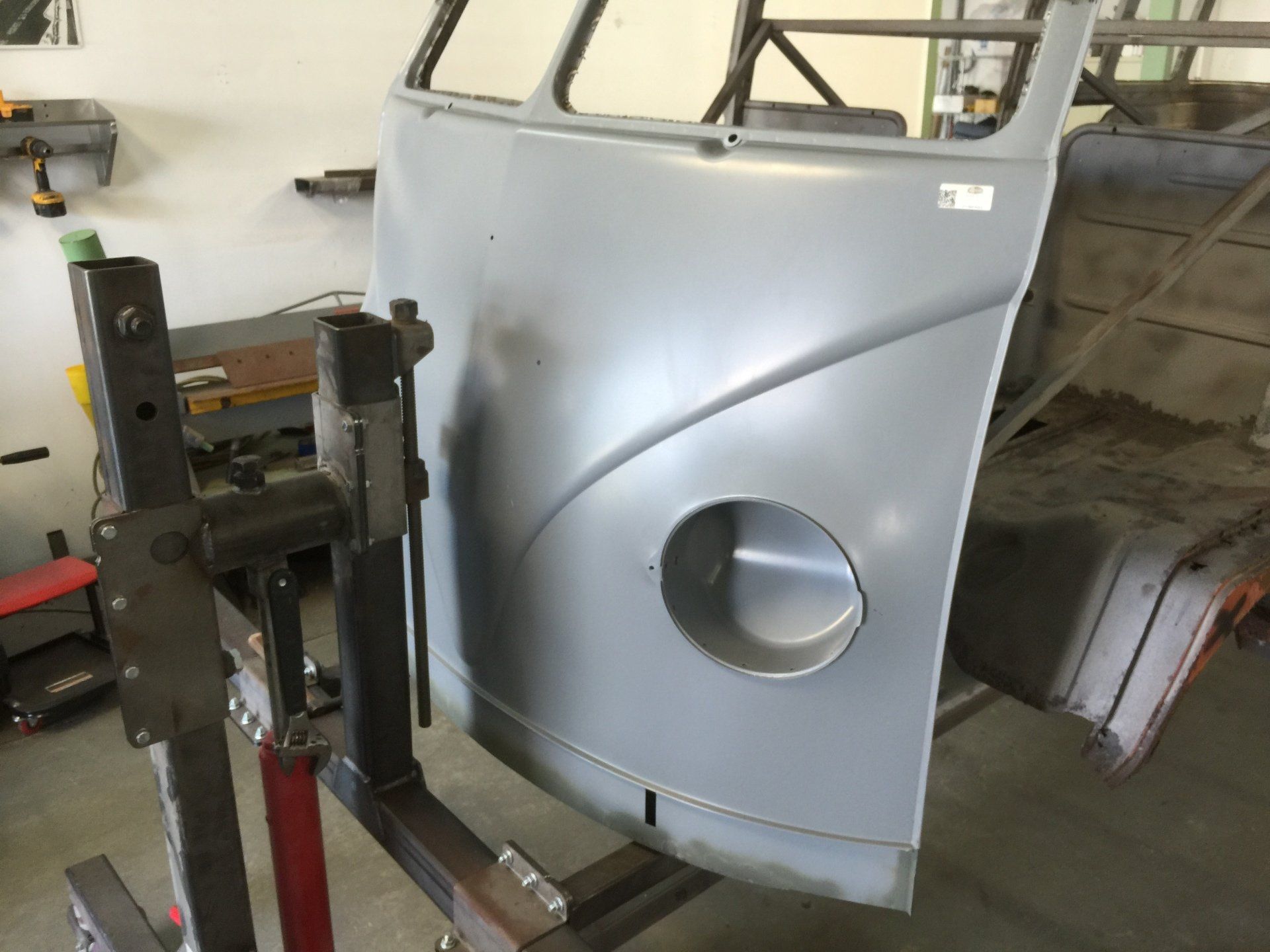 Gray car body panel mounted on a metal frame in a workshop