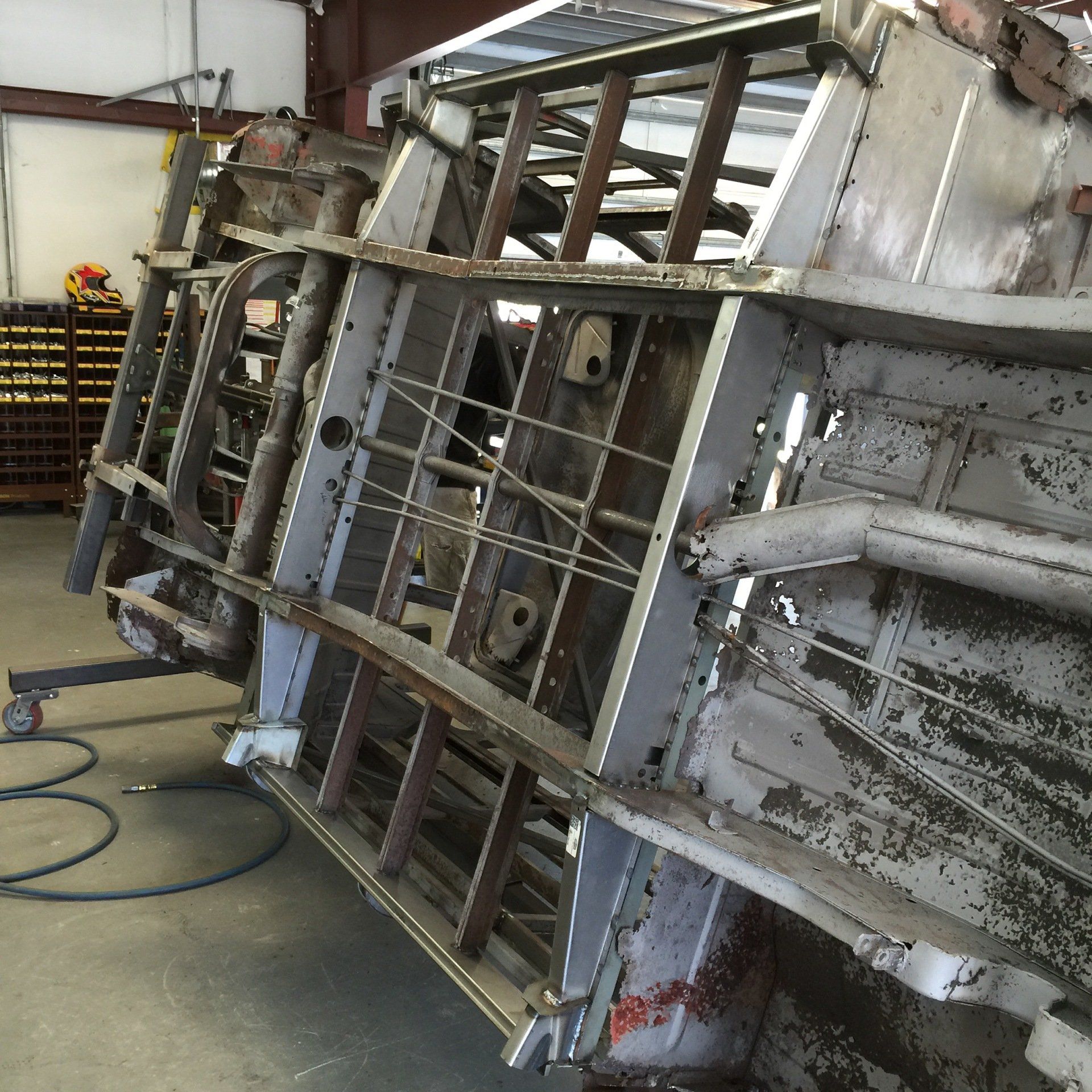 Metal industrial frame or machinery section lying on its side in a workshop, with hoses on the floor.