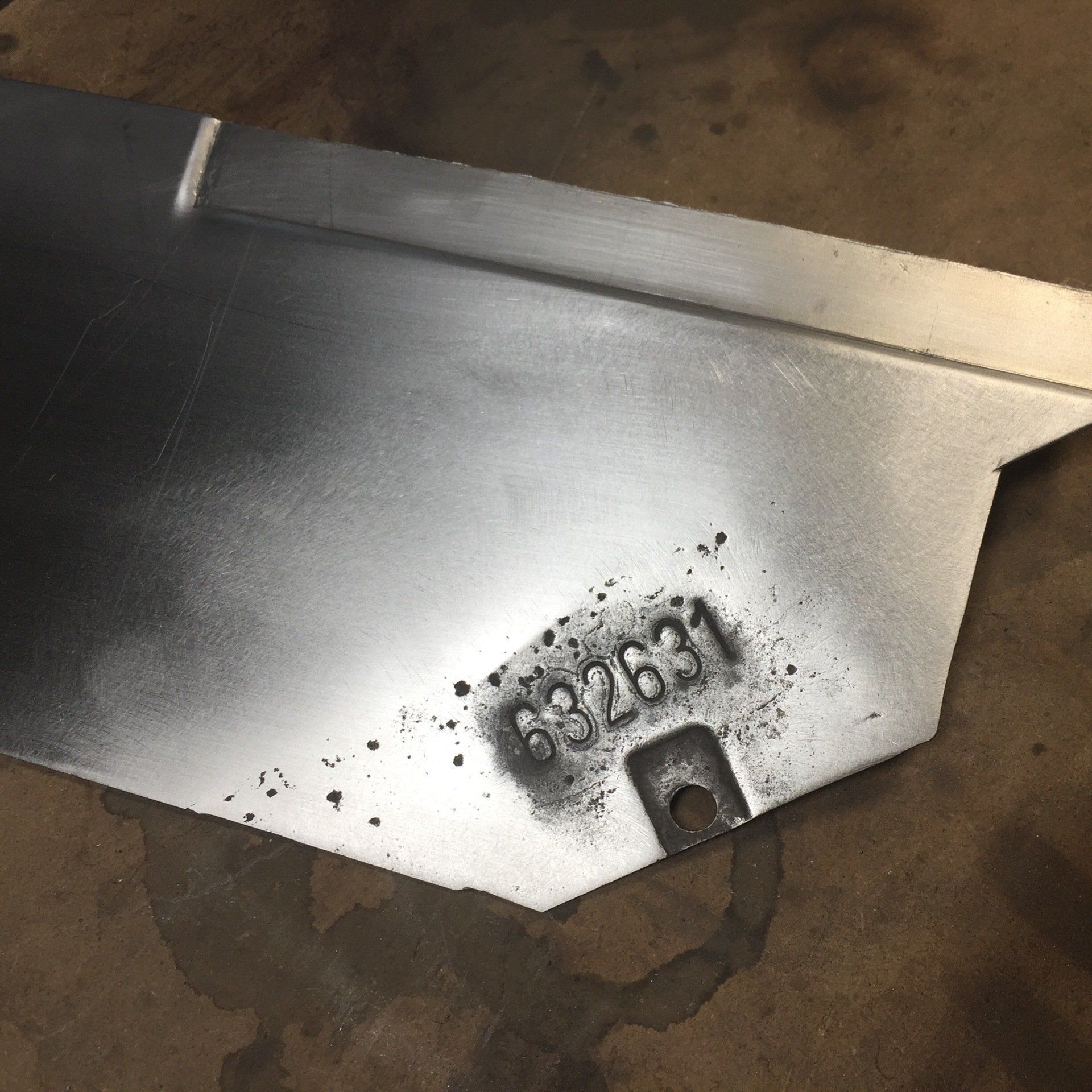 Close-up of a silver metal surface with stamped numbers and a small dark cutout.