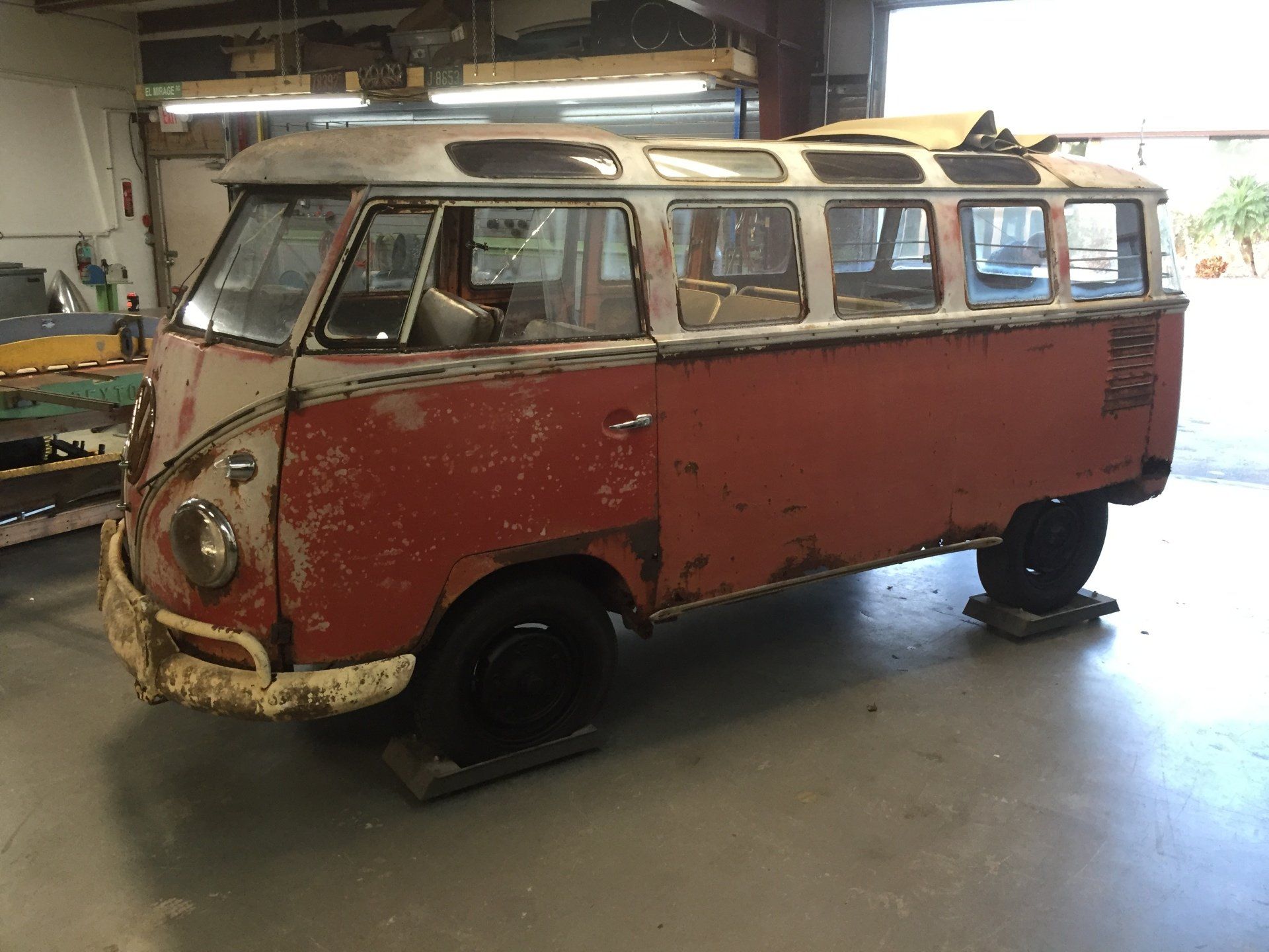 Rusty red vintage Volkswagen van in a garage, with worn paint and missing front bumper.