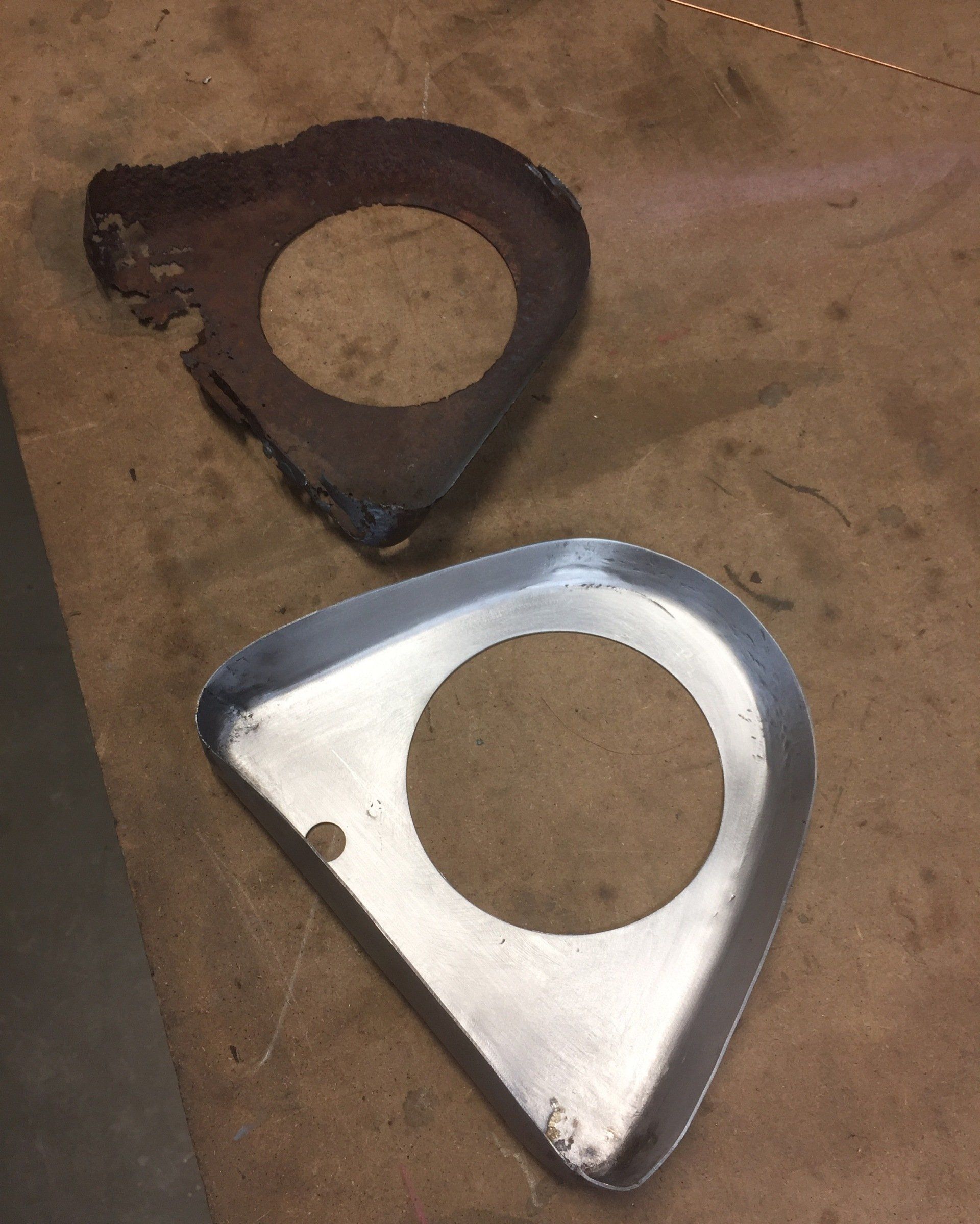 Two triangular metal flanges, one rusty and one shiny silver, on a brown surface.