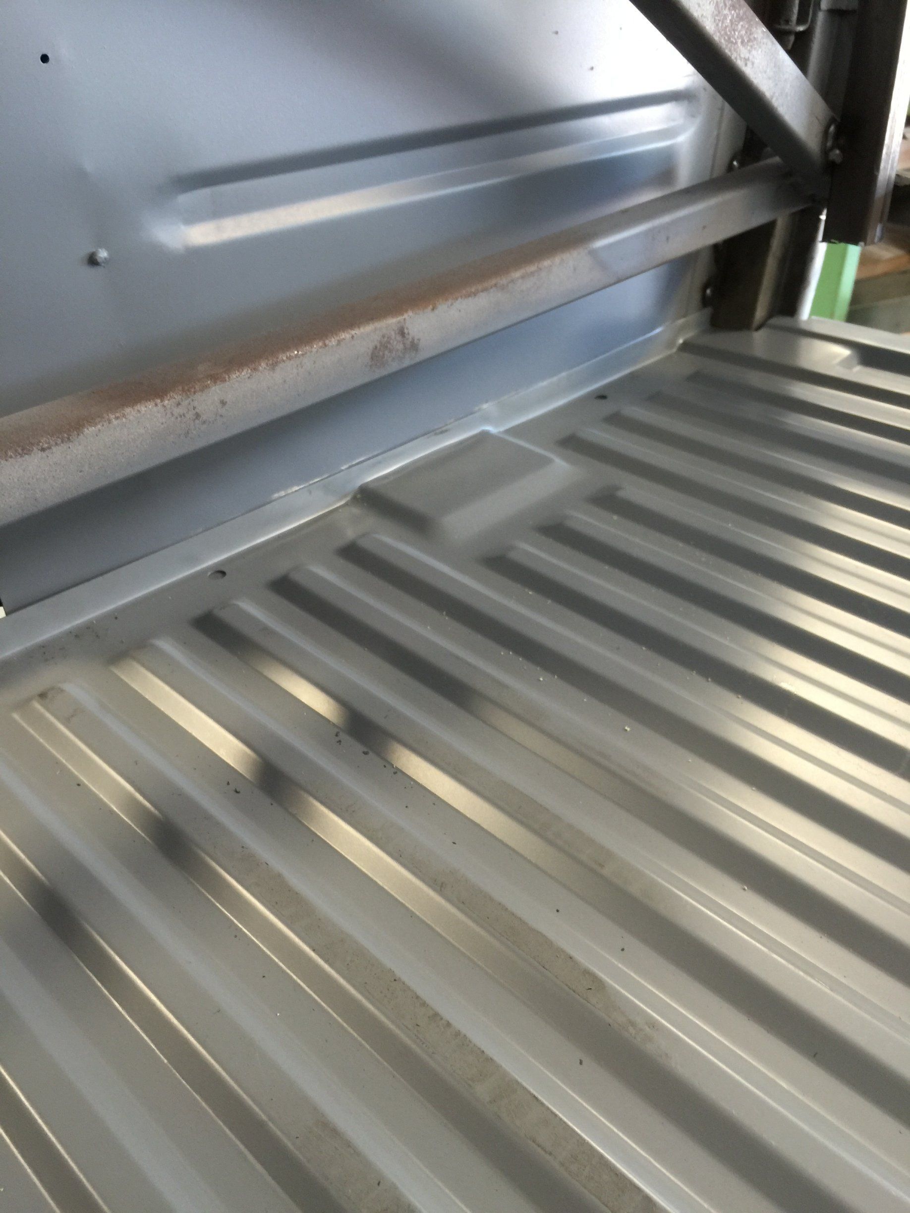 Close-up of a silver metal truck bed liner with ridged floor and side panel.