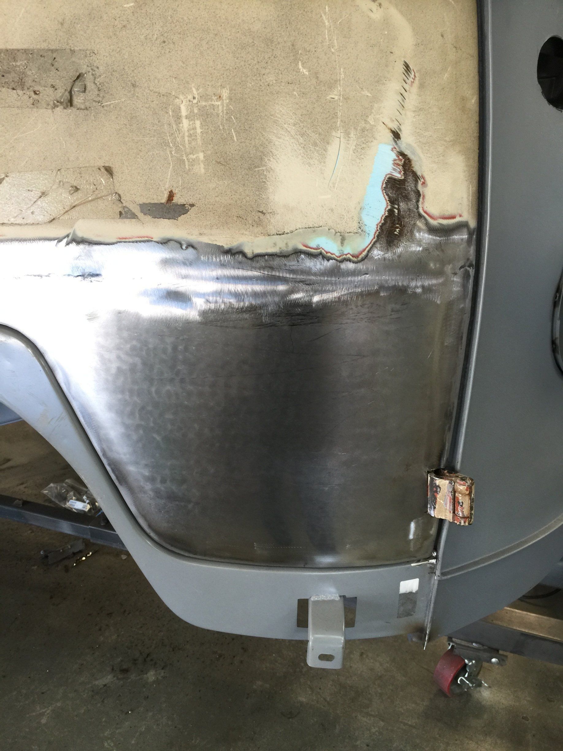 Close-up of a worn metal container or tank with rust, peeling paint, and a gray bracket at the bottom.