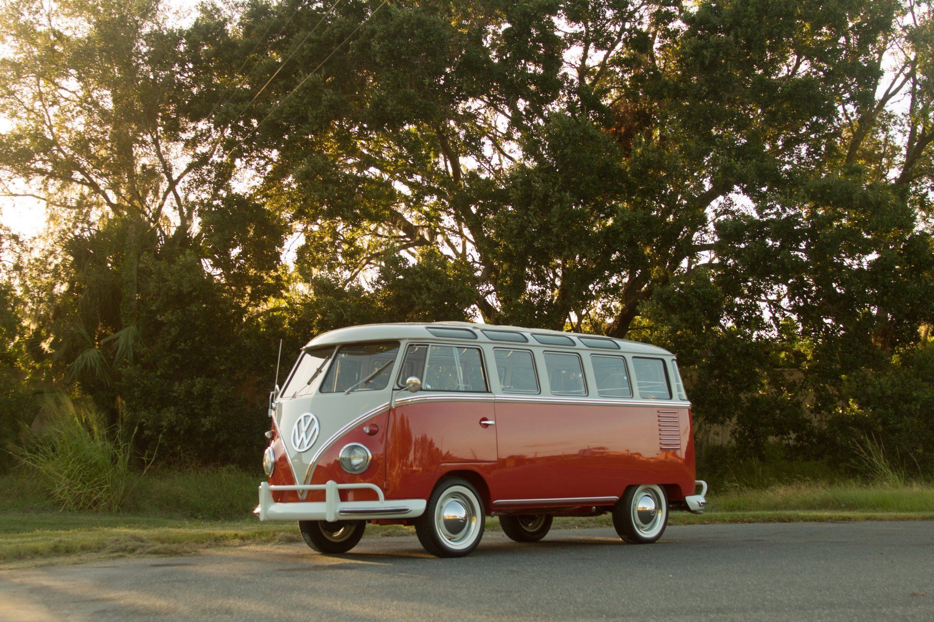 Red and white vintage van parked on a road beside trees at sunset