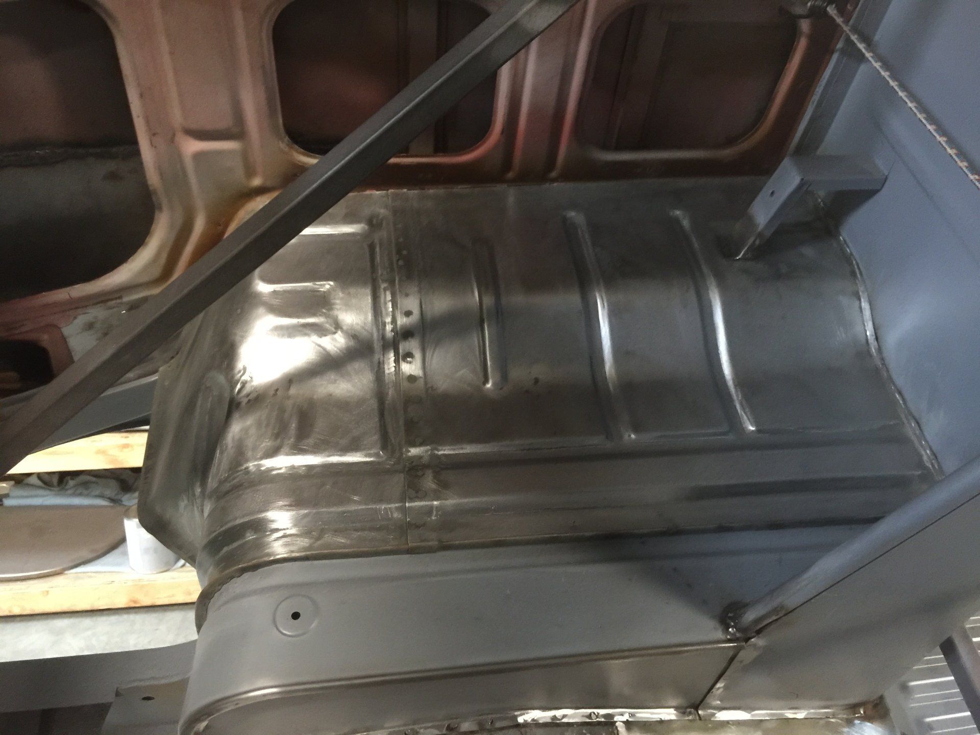 Shiny metal undercarriage panels and support beams beneath a vehicle, with road light visible at left