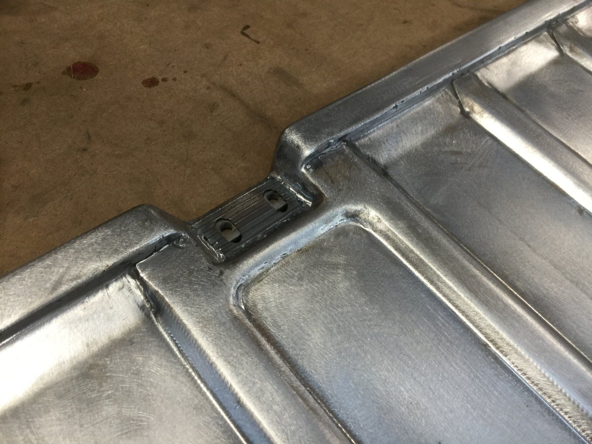 Close-up of two silver metal panels joined by a small black hinge on a brown surface
