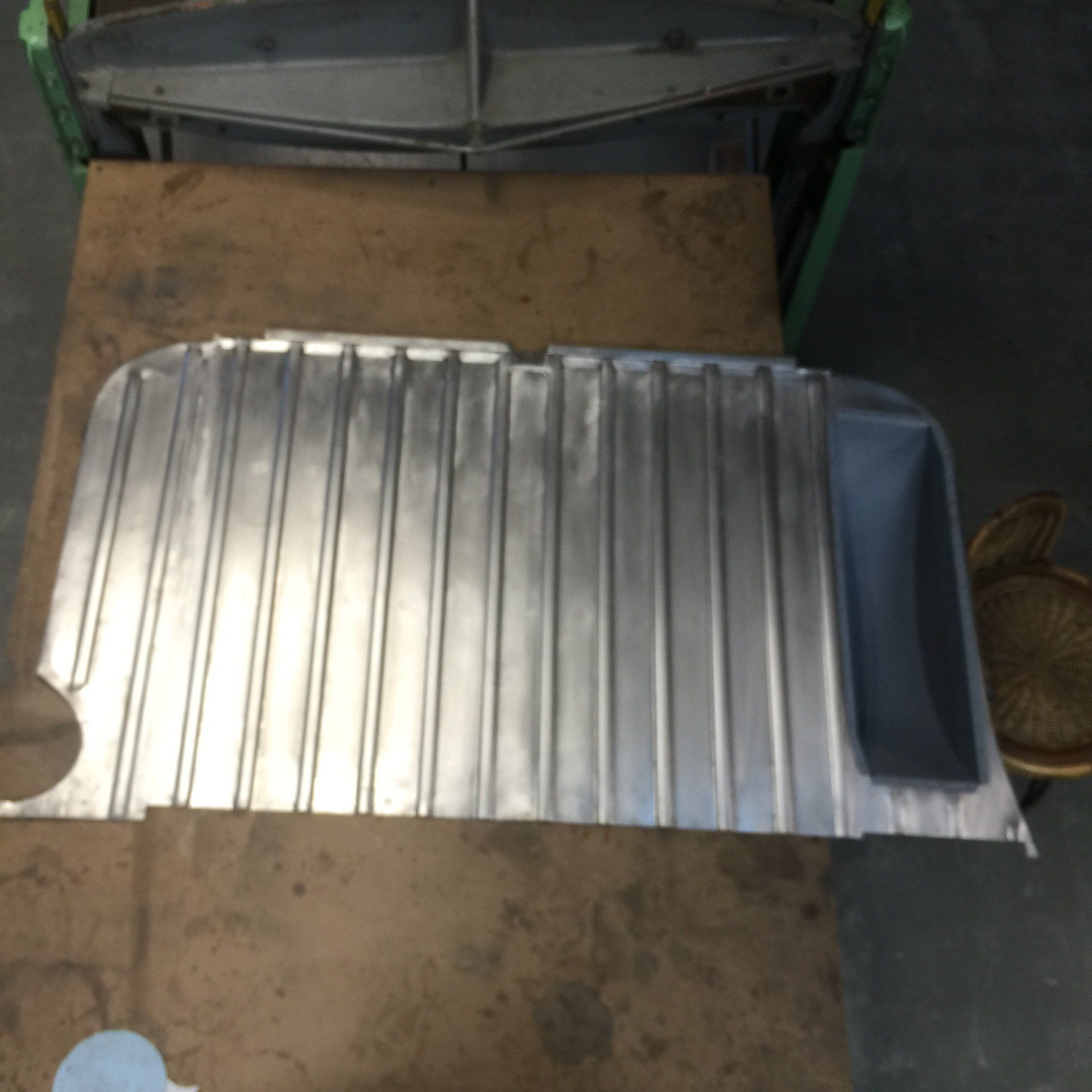 Metal ribbed panel with a dark blue padded end, lying on a worn wooden surface indoors.