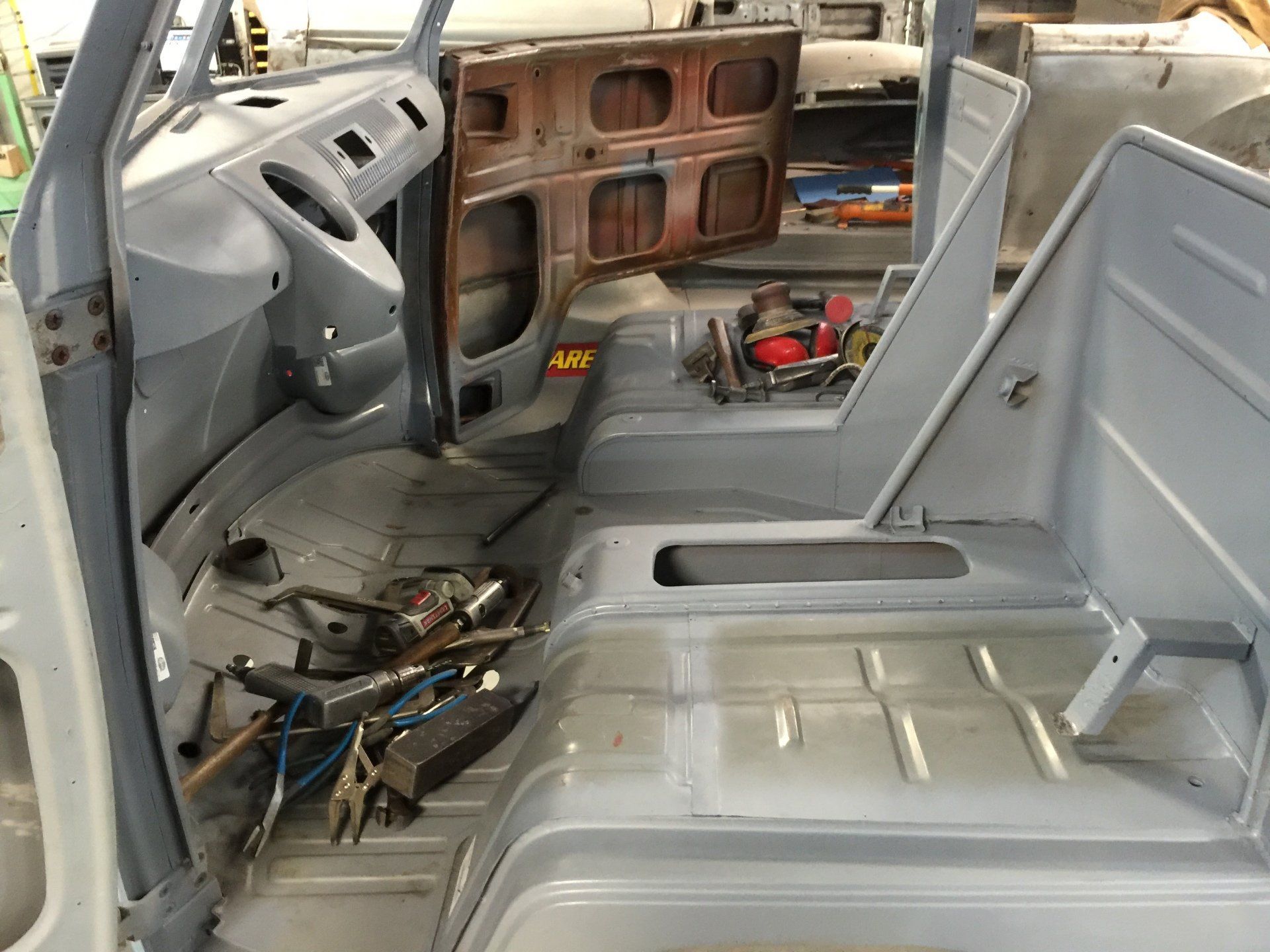 Car interior stripped for repair, with exposed metal, removed seats, and tools scattered on the floor.