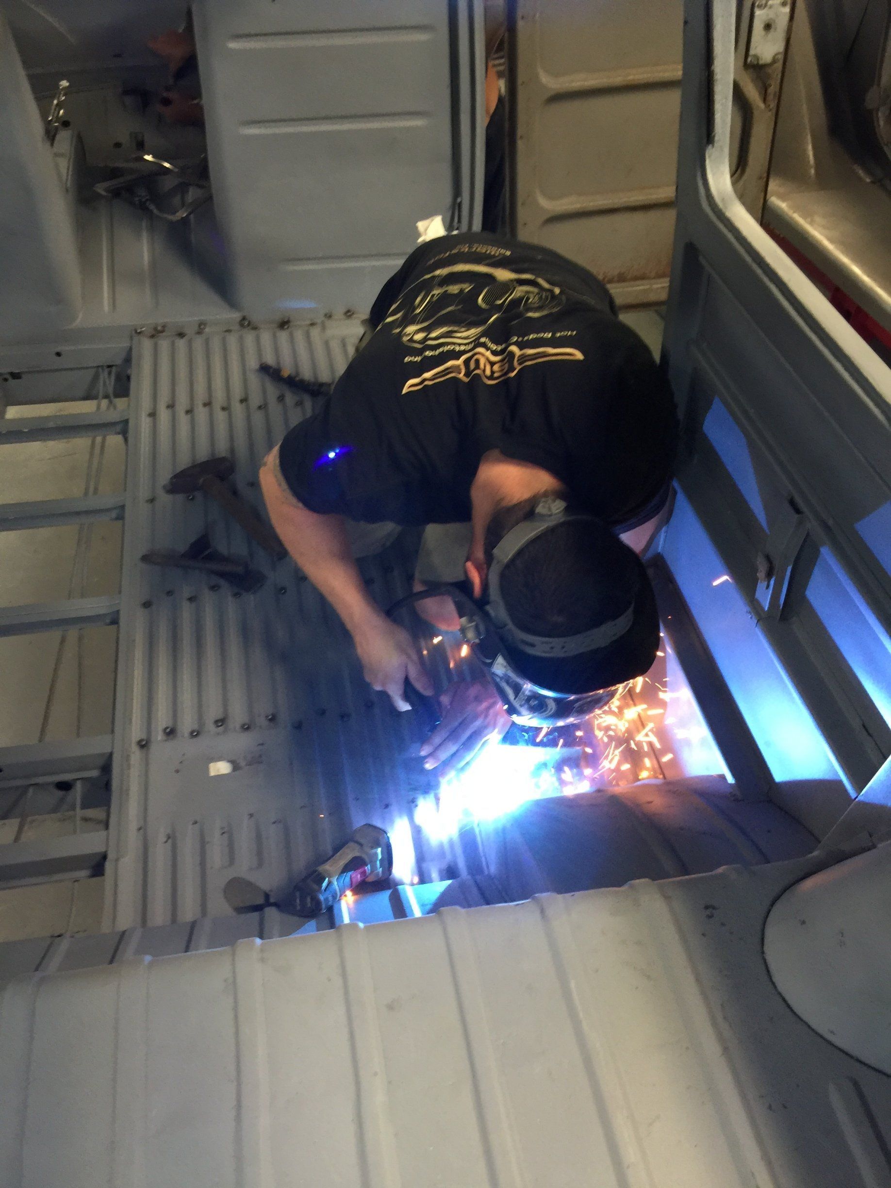 Person welding inside a metal interior, bright blue arc and sparks illuminating the workspace.