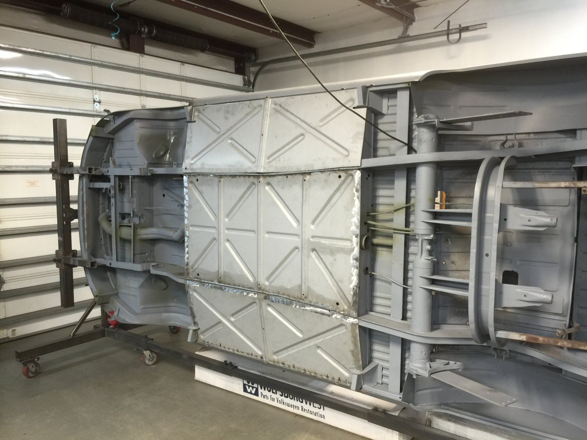 Upside-down aircraft fuselage section in a hangar, with exposed metal panels and structural framework