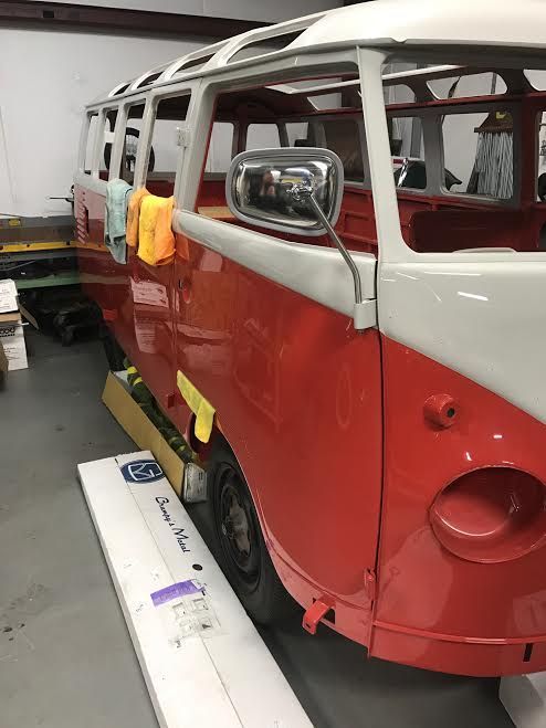 Red and white vintage van body in a workshop, with exposed frame and masking tape.