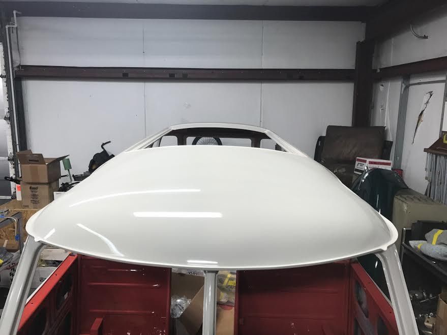 White car body shell in a garage with its hood propped open over a red chassis.