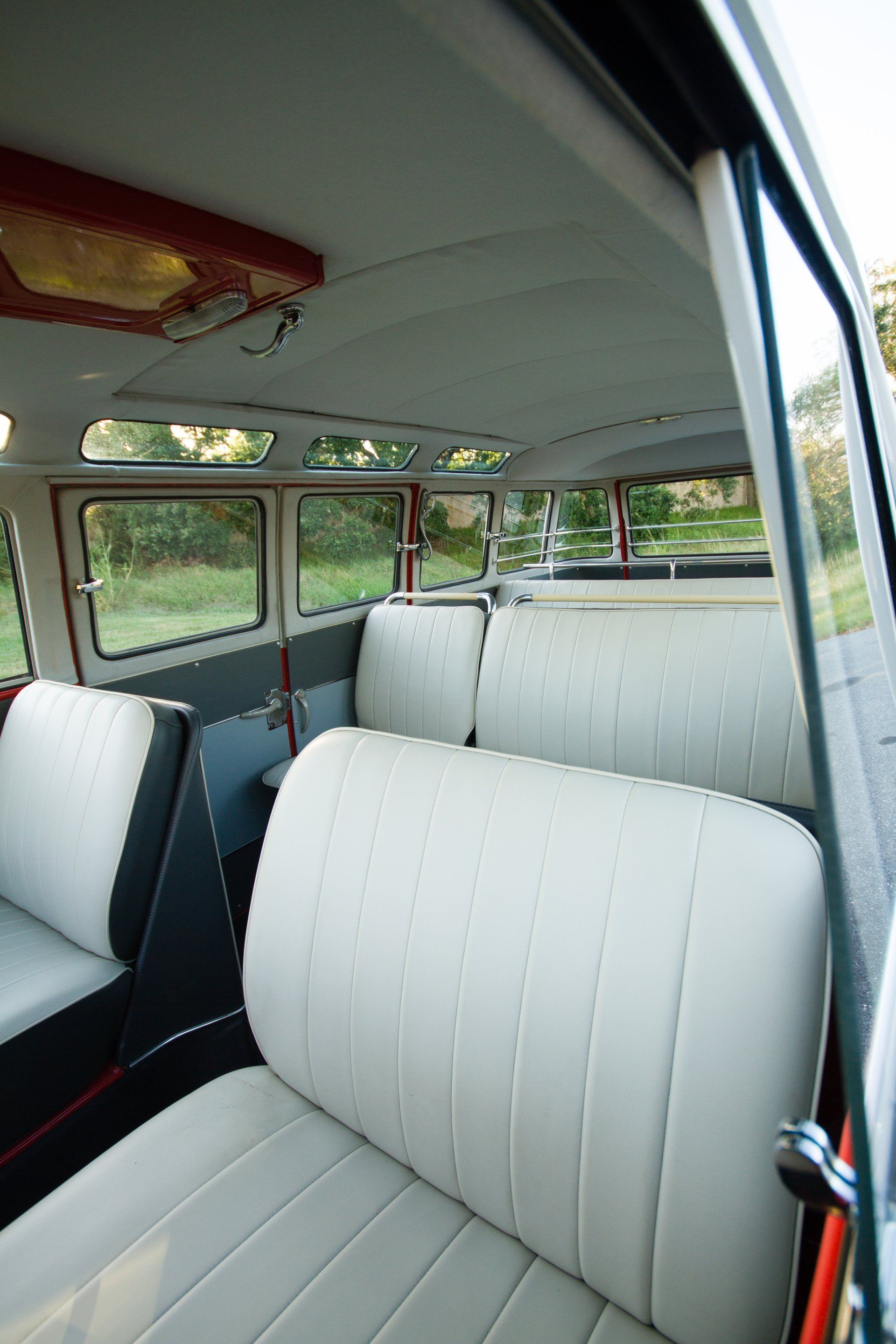 Inside a vintage bus with white seats and open windows, showing the interior seating area.