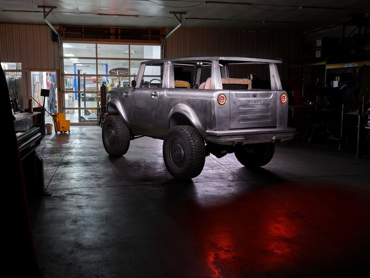 Custom silver off-road SUV parked in a dim garage with red light reflection on the floor