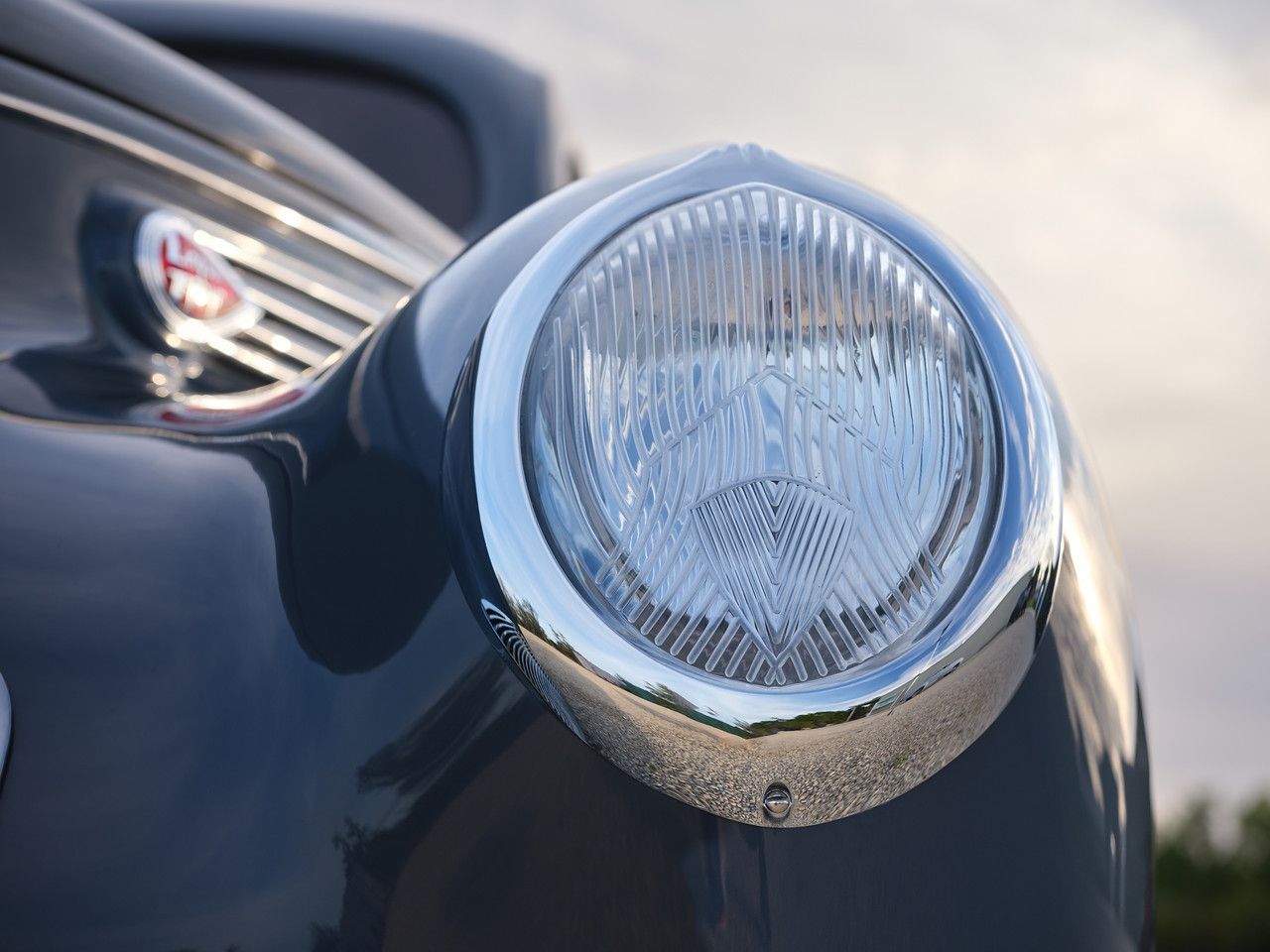 Close-up of a classic car’s chrome headlight and glossy dark-blue fender
