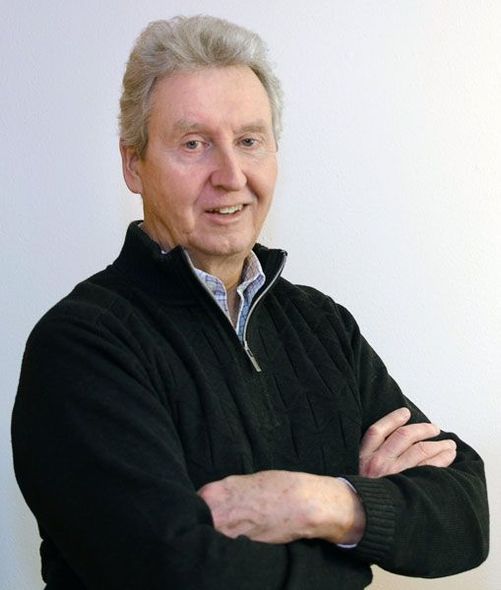 Portrait of a smiling man in a black zip-up sweater, arms crossed against a plain white background