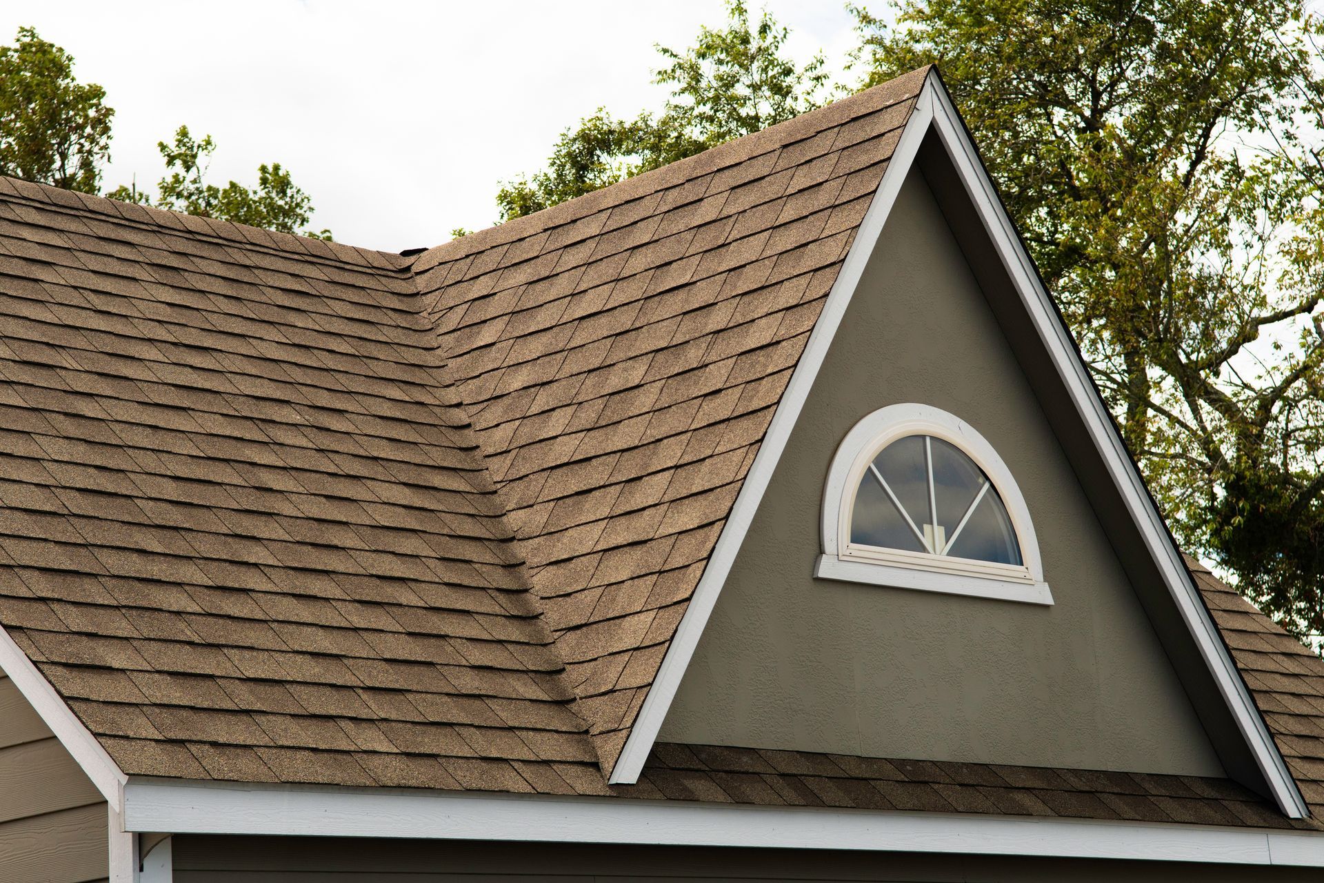 A residential home with a sloped roof covered in clean asphalt shingles and a small attic window.