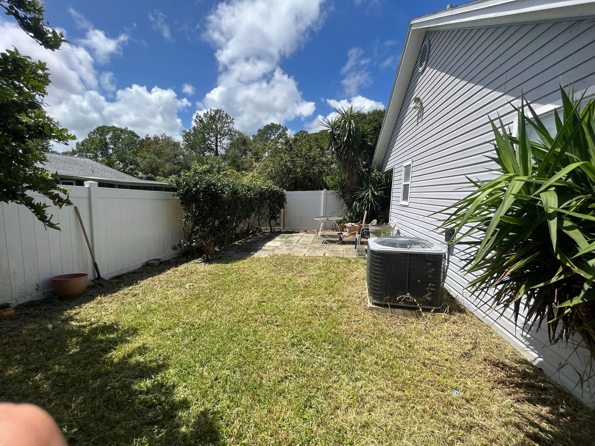 The backyard of a house with a white fence and a large lawn.